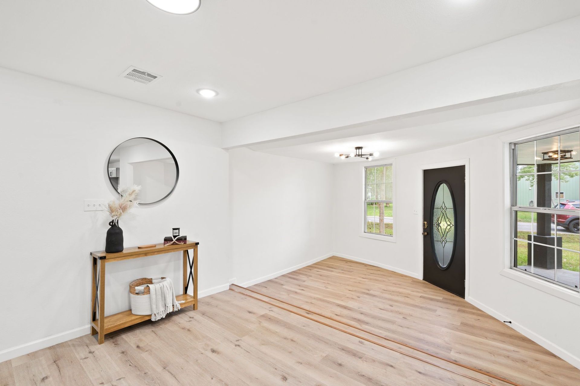 A living room with hardwood floors , white walls , a mirror and a door.