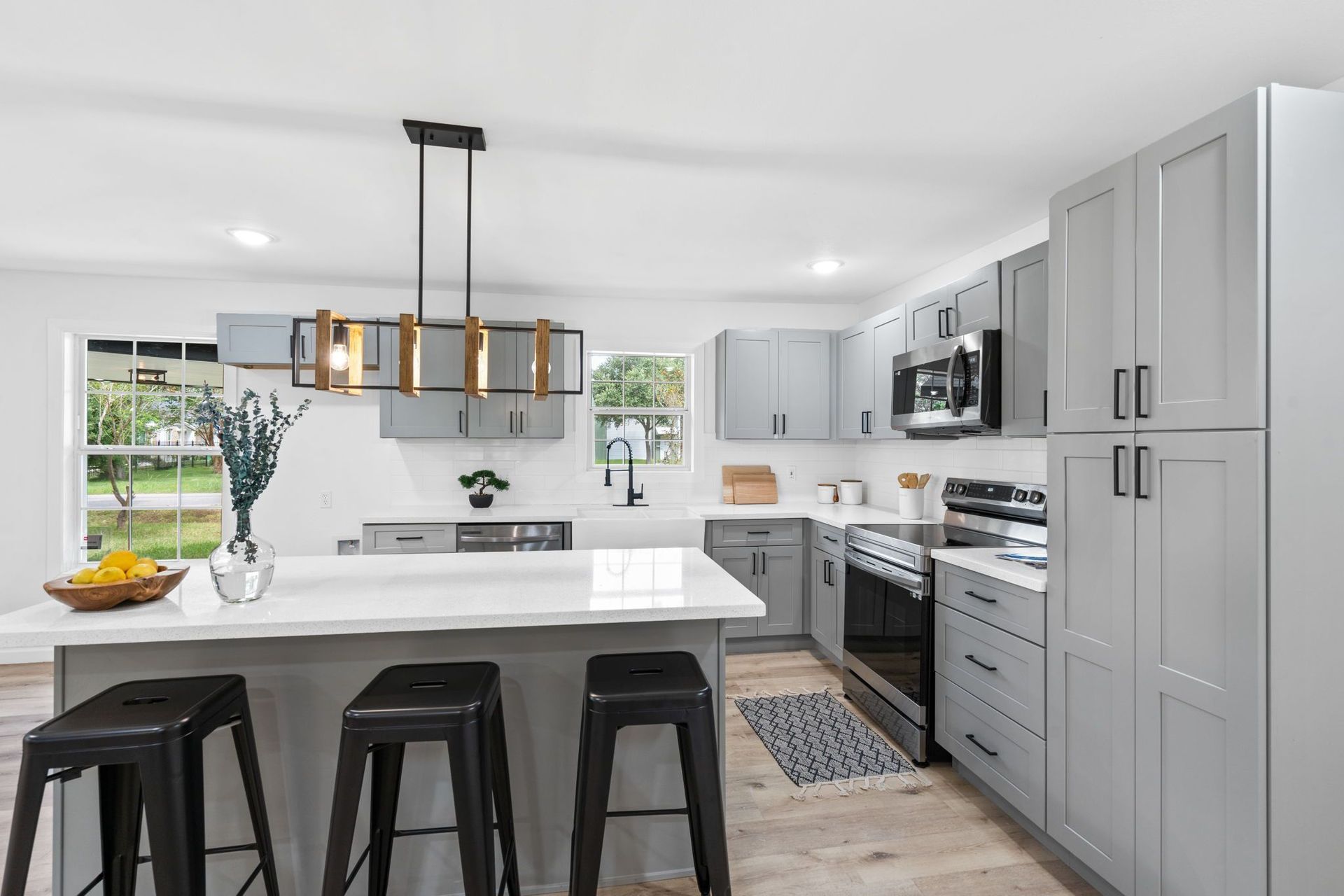 A kitchen with gray cabinets , black stools and a large island.