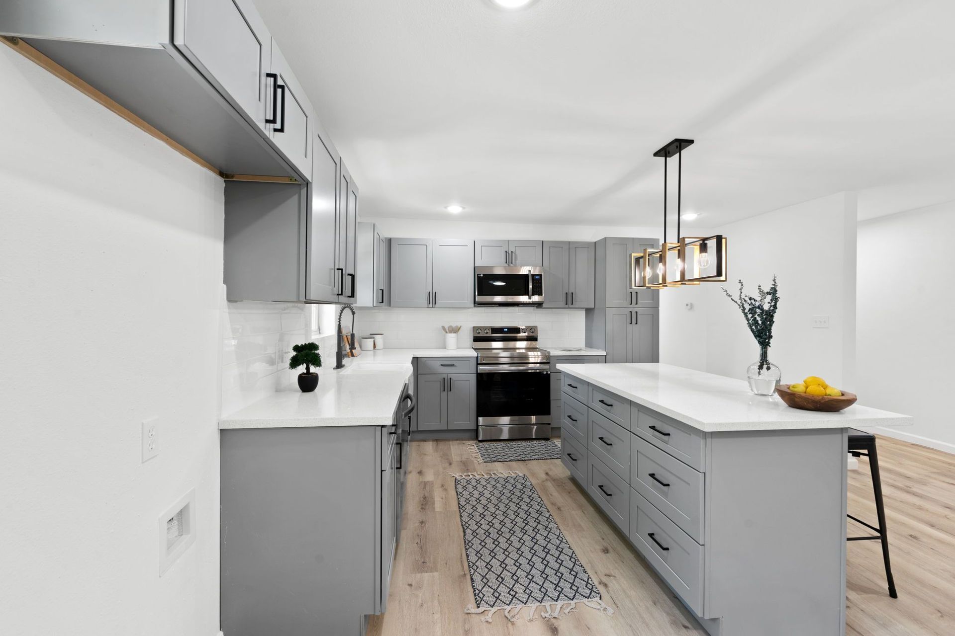 A kitchen with gray cabinets , white counter tops , stainless steel appliances and a large island.