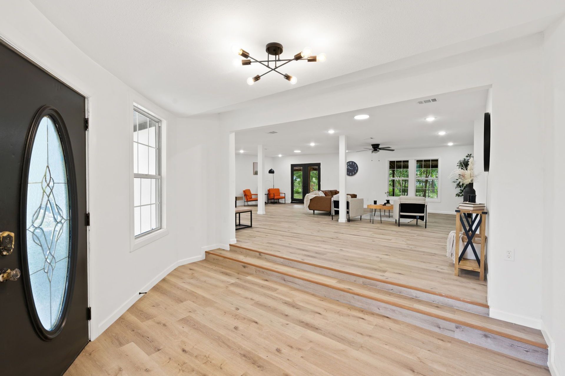 A hallway with hardwood floors and a black door leading to a living room.