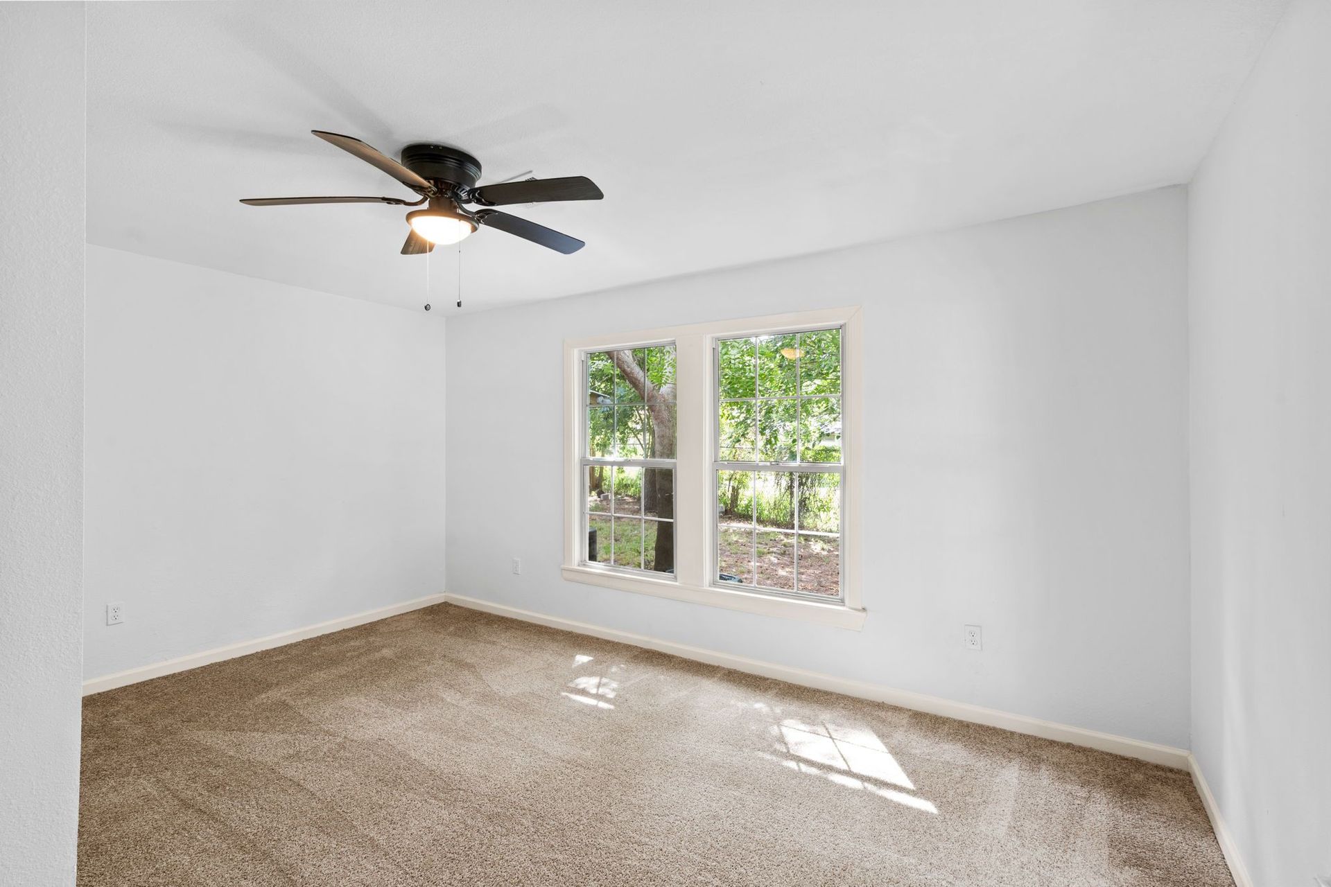 An empty bedroom with a ceiling fan and two windows.
