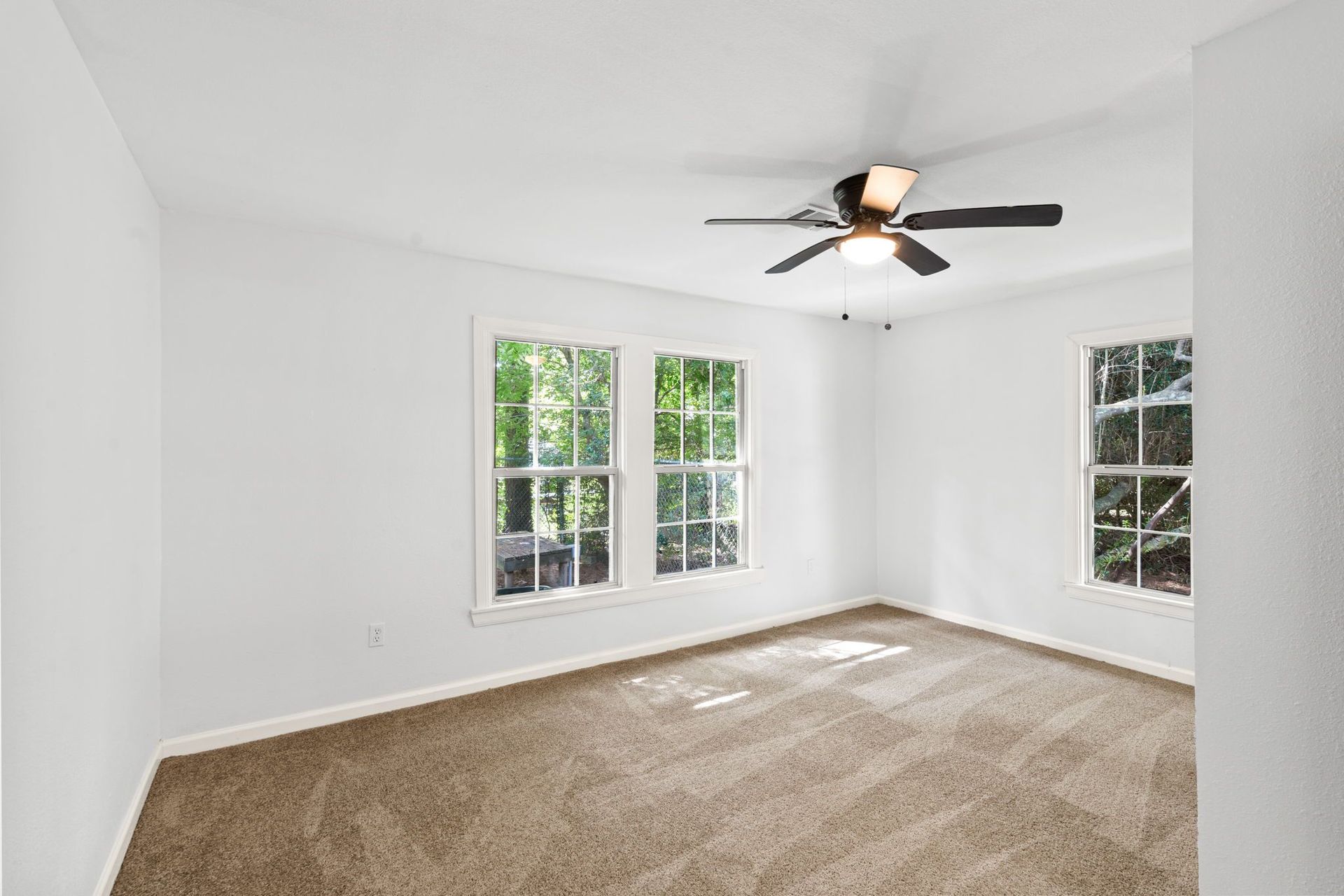 An empty bedroom with a ceiling fan and two windows.