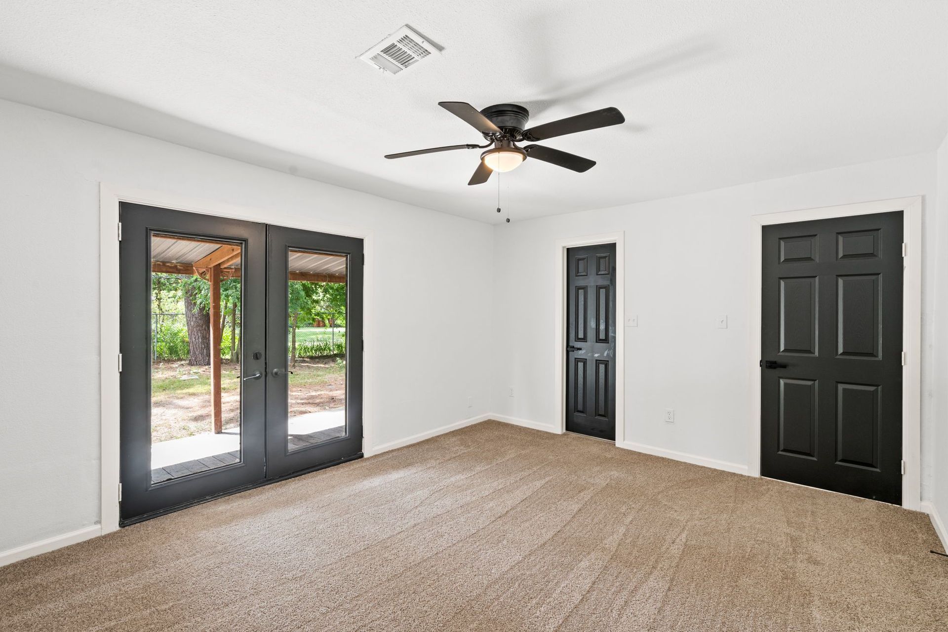 An empty room with a ceiling fan and black doors.