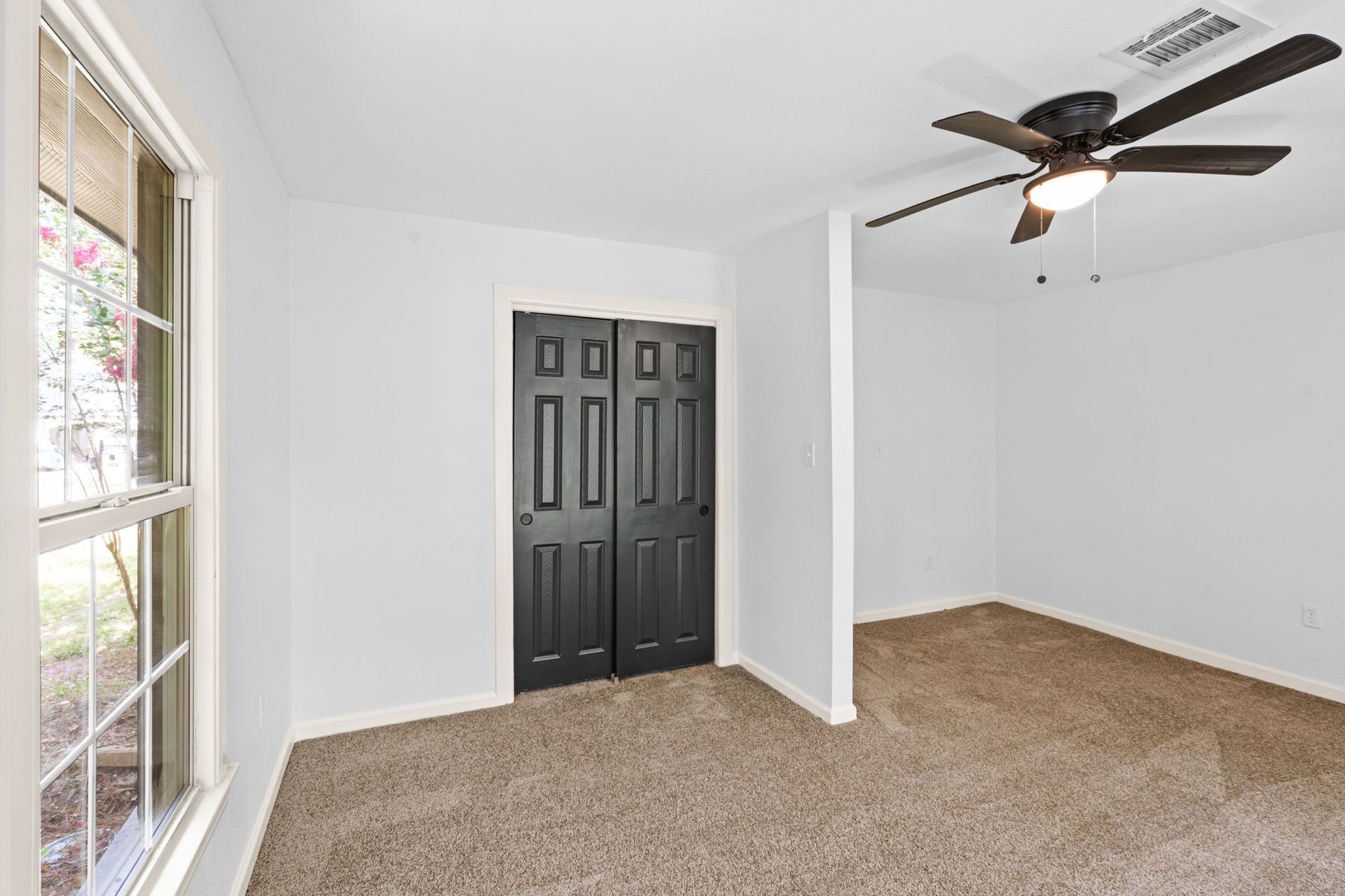 An empty room with a ceiling fan and a window.