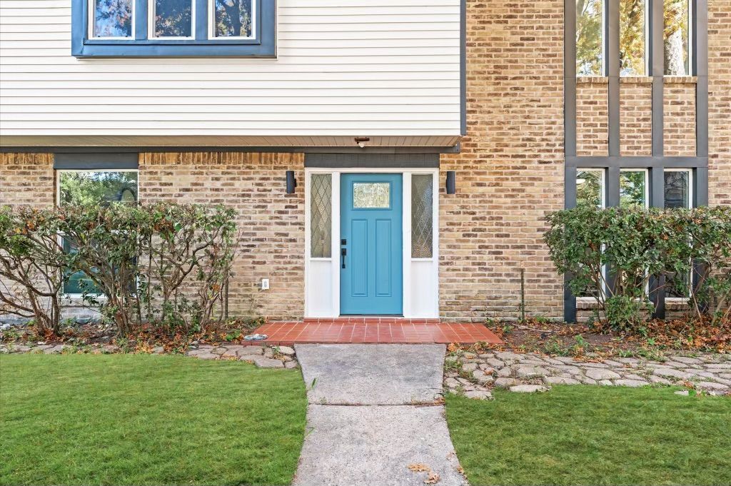 The front of a brick house with a blue door and a walkway leading to it.