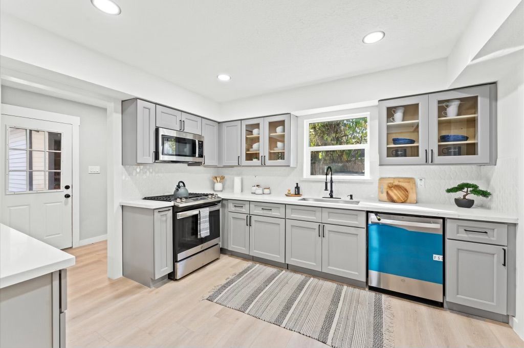 Modern gray kitchen with stainless steel appliances, a blue dishwasher, and a small rug.