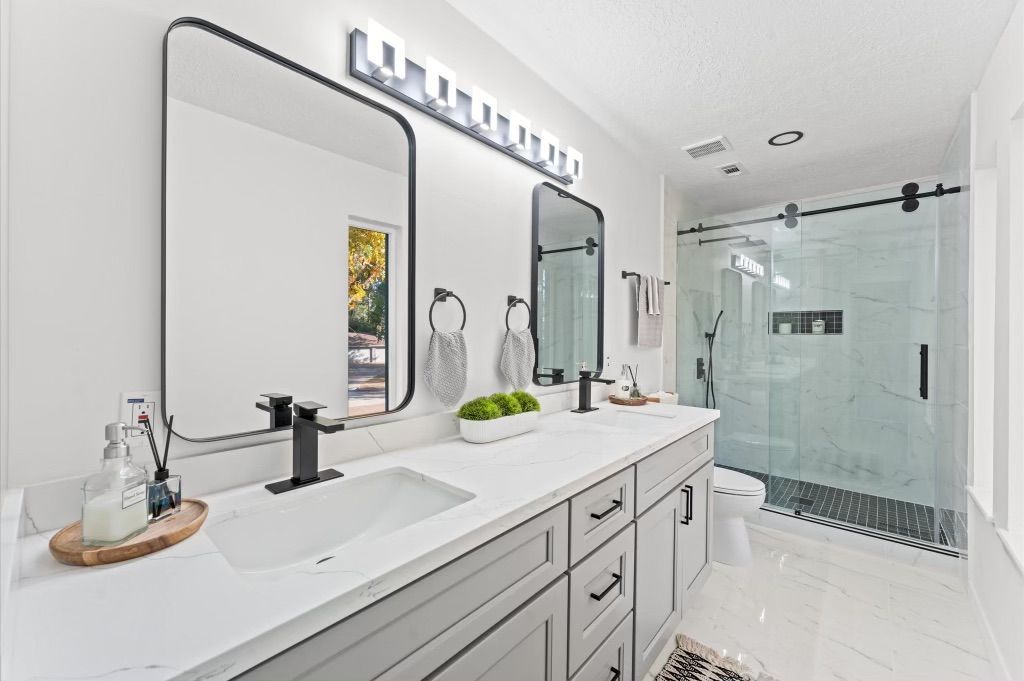 A bathroom with two sinks , two mirrors and a walk in shower.