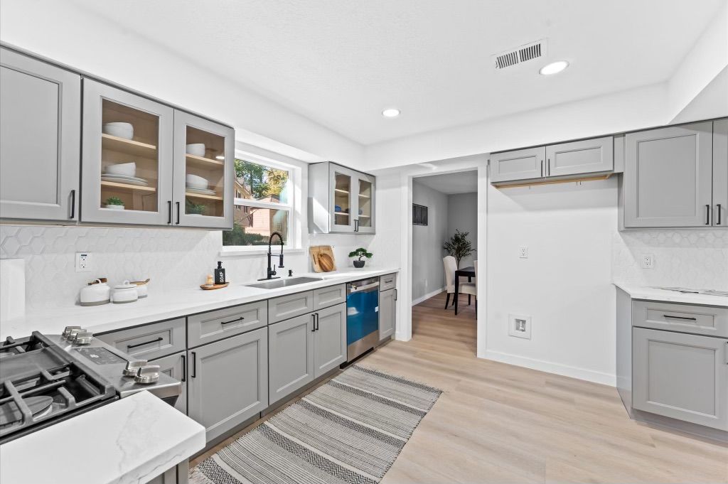 A kitchen with gray cabinets , white counter tops , and stainless steel appliances.