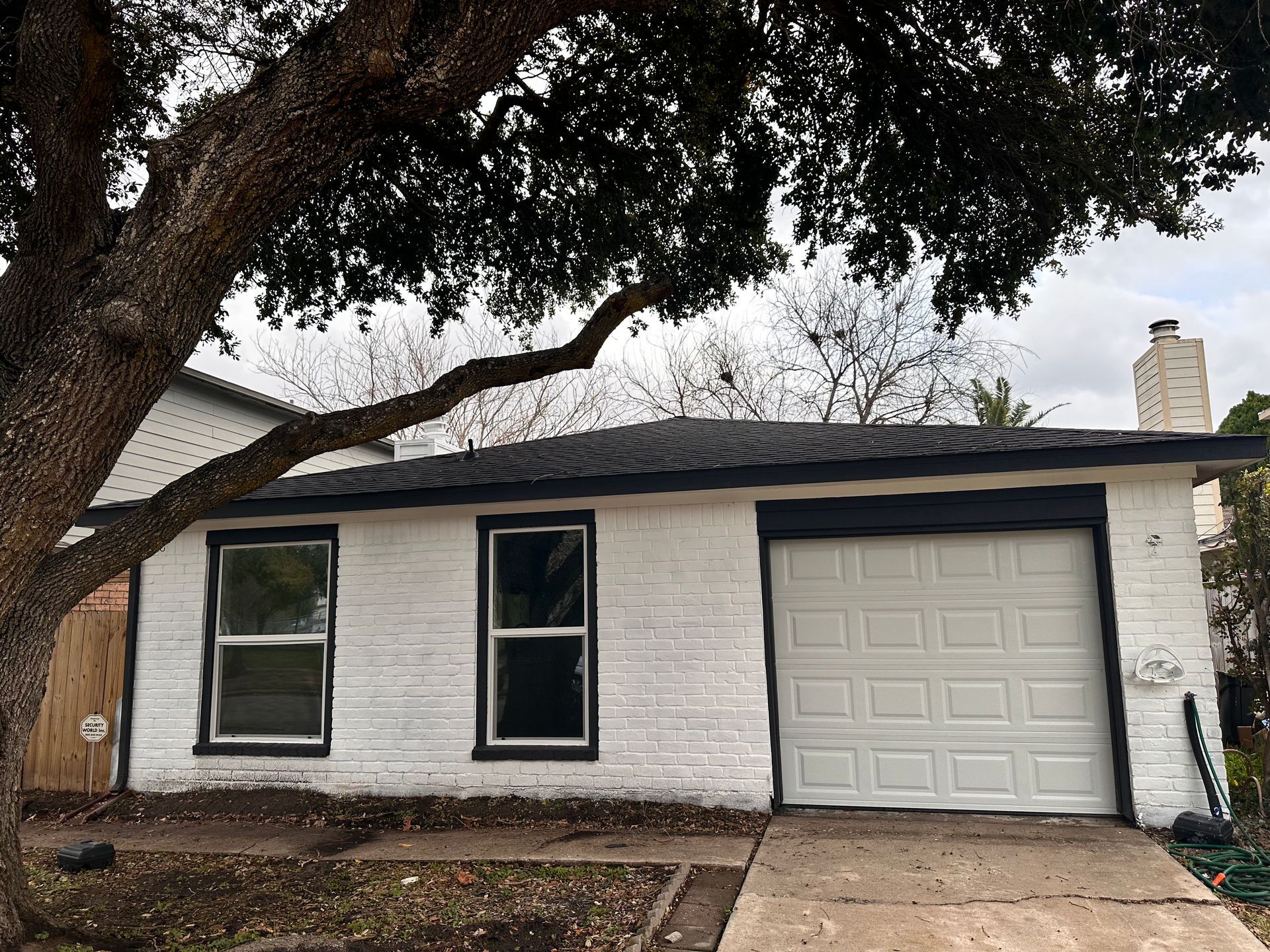 A white brick house with a white garage door and a tree in front of it.