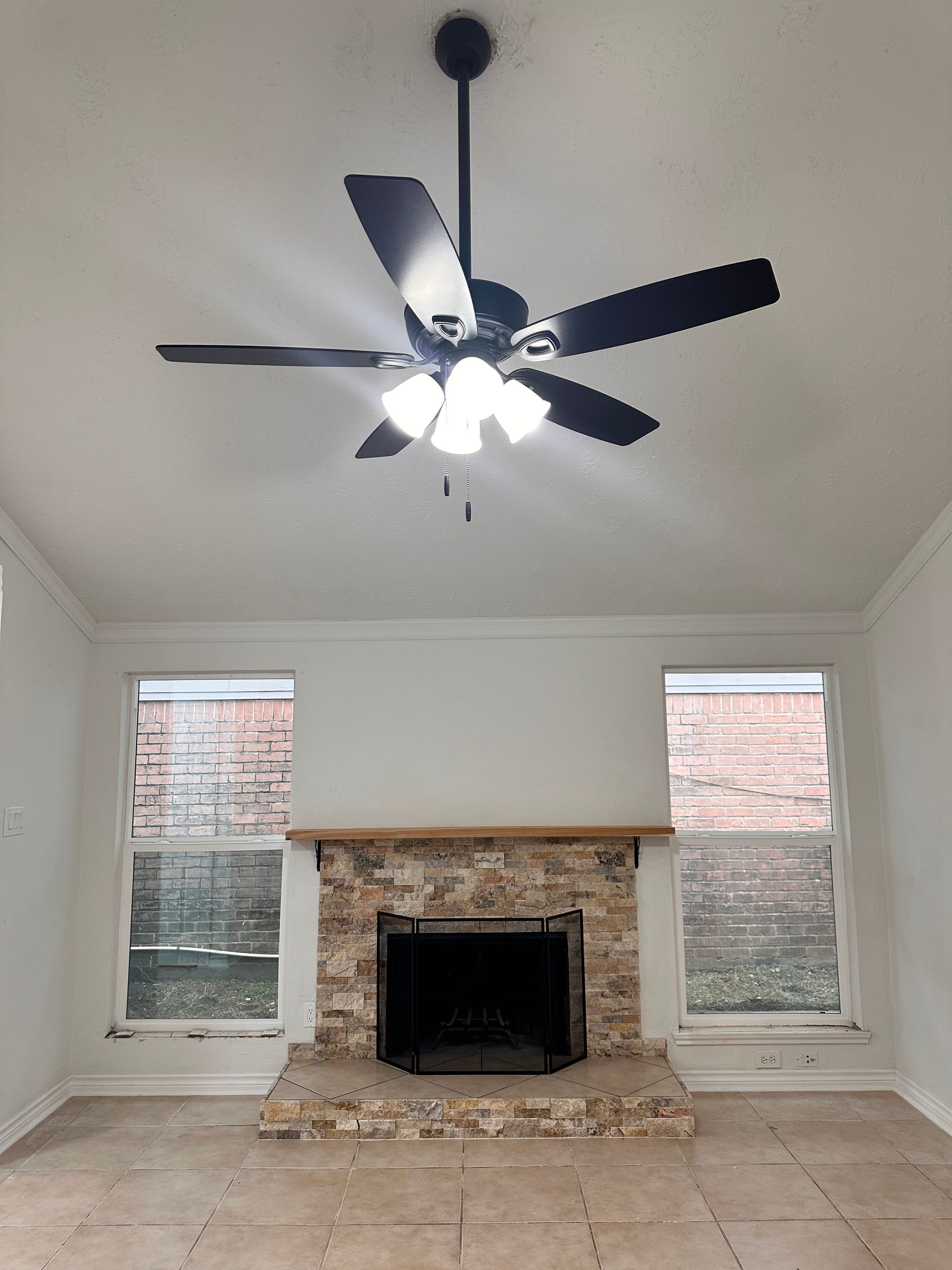 An empty living room with a fireplace and ceiling fan