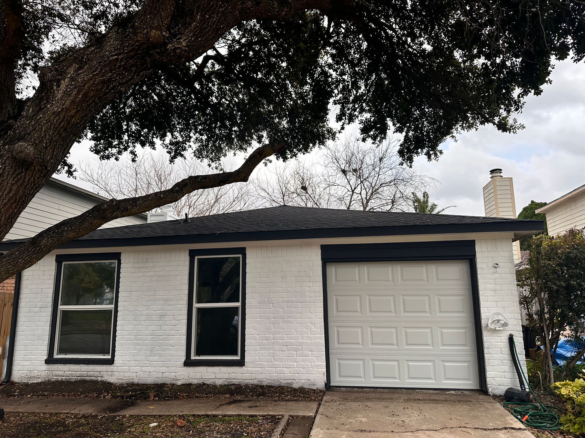 A white brick house with a white garage door and a tree in front of it.