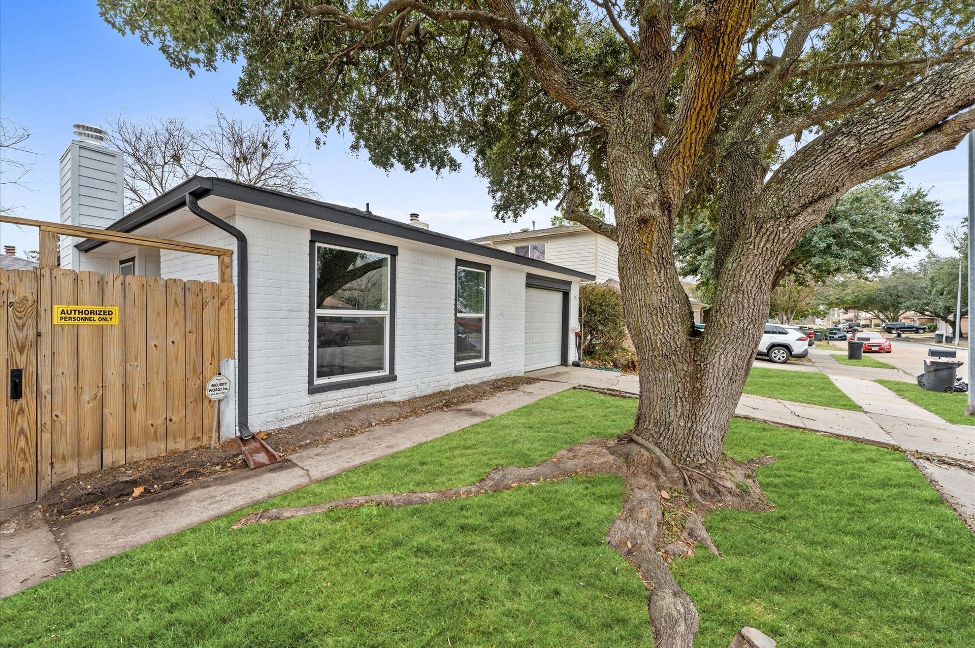 A white house with a wooden fence and a tree in front of it.