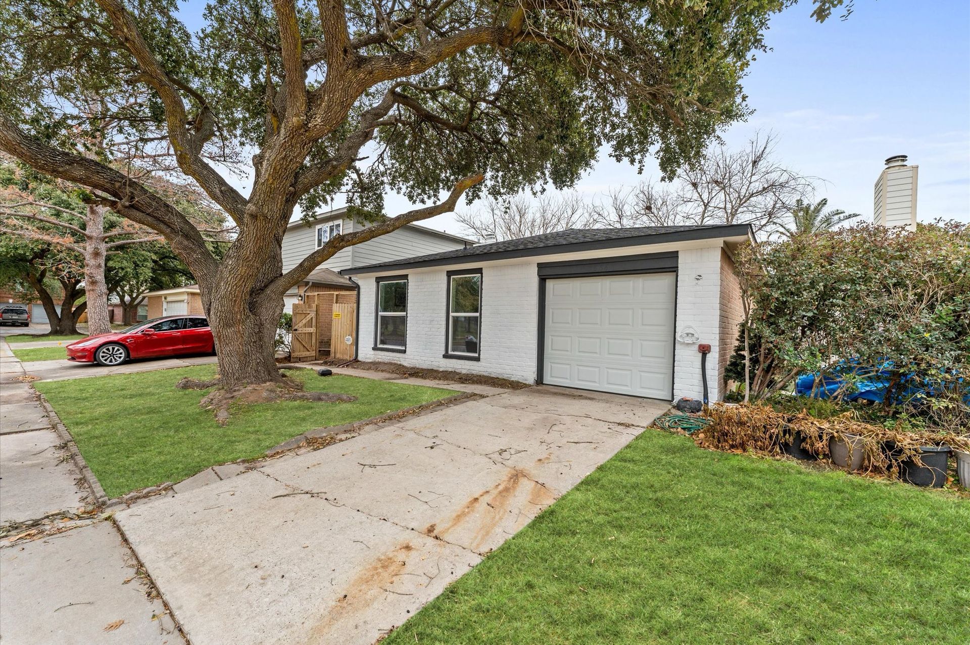 House with garage and driveway on a green lawn; a red car is parked in the street.