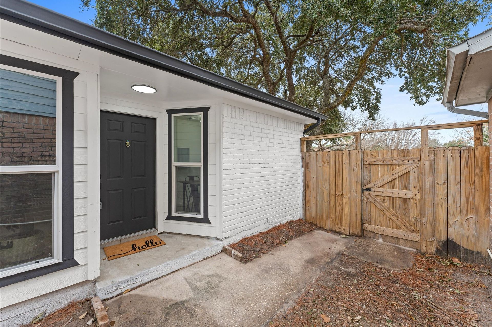 A white brick house with a black door and a wooden fence.