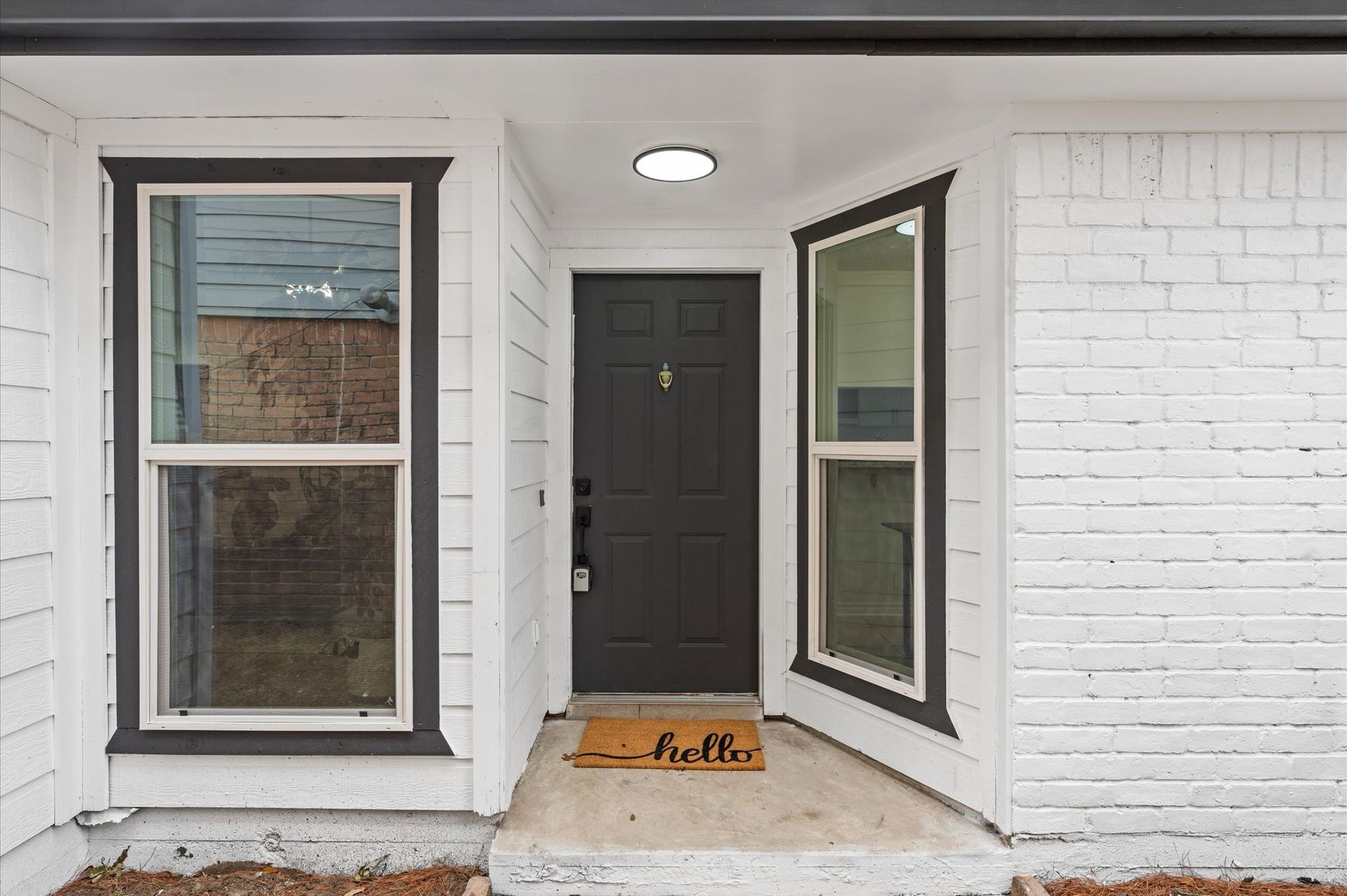 A white brick house with a black door and two windows.