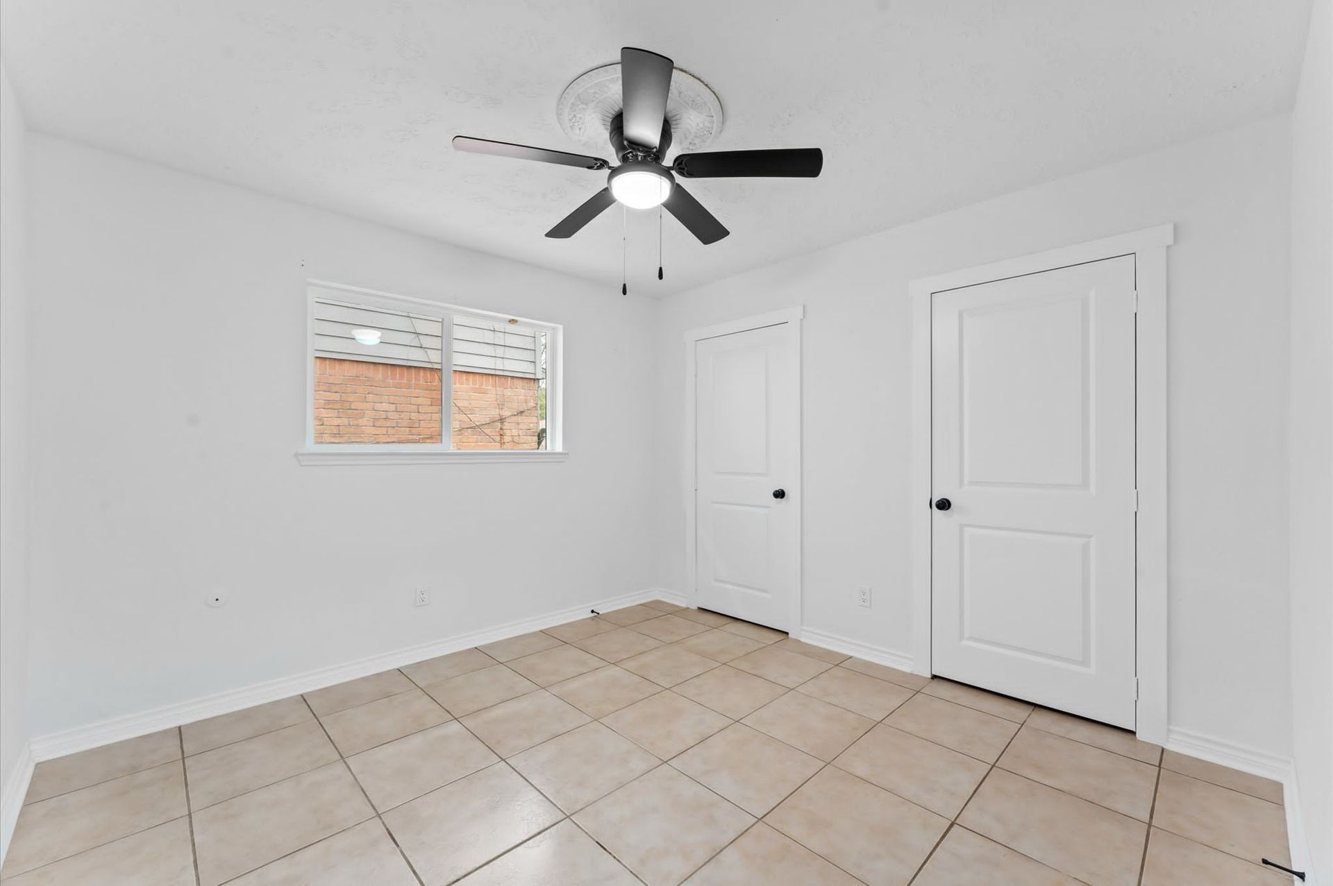 An empty room with a ceiling fan and a window.