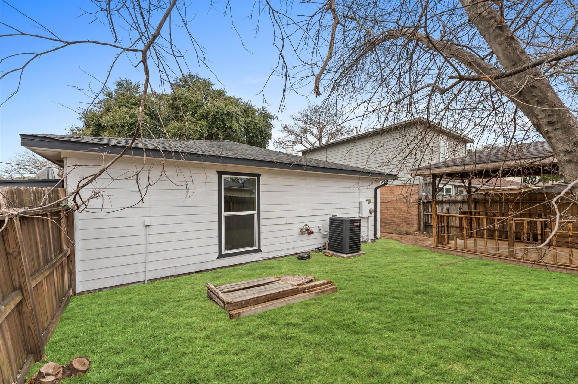 The backyard of a house with a large lawn and a wooden fence.