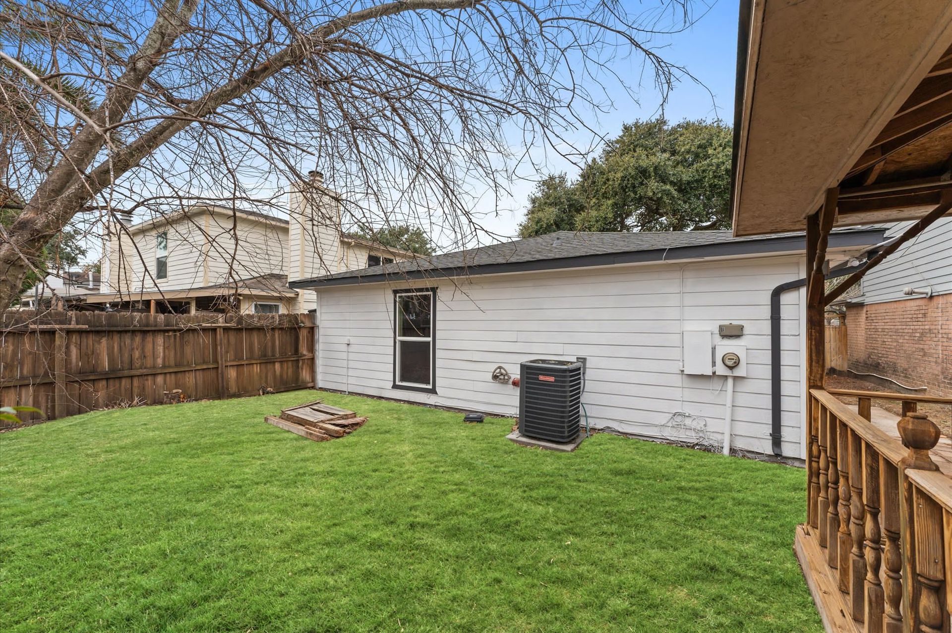 The backyard of a house with a large lawn and a wooden fence.
