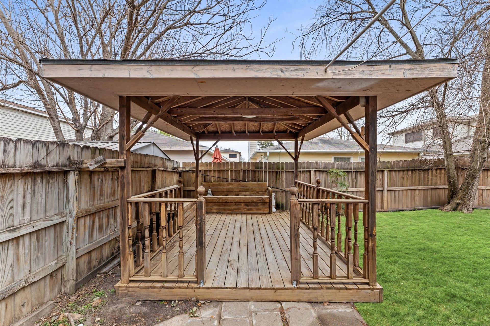 A wooden gazebo in the backyard of a house with a wooden fence.