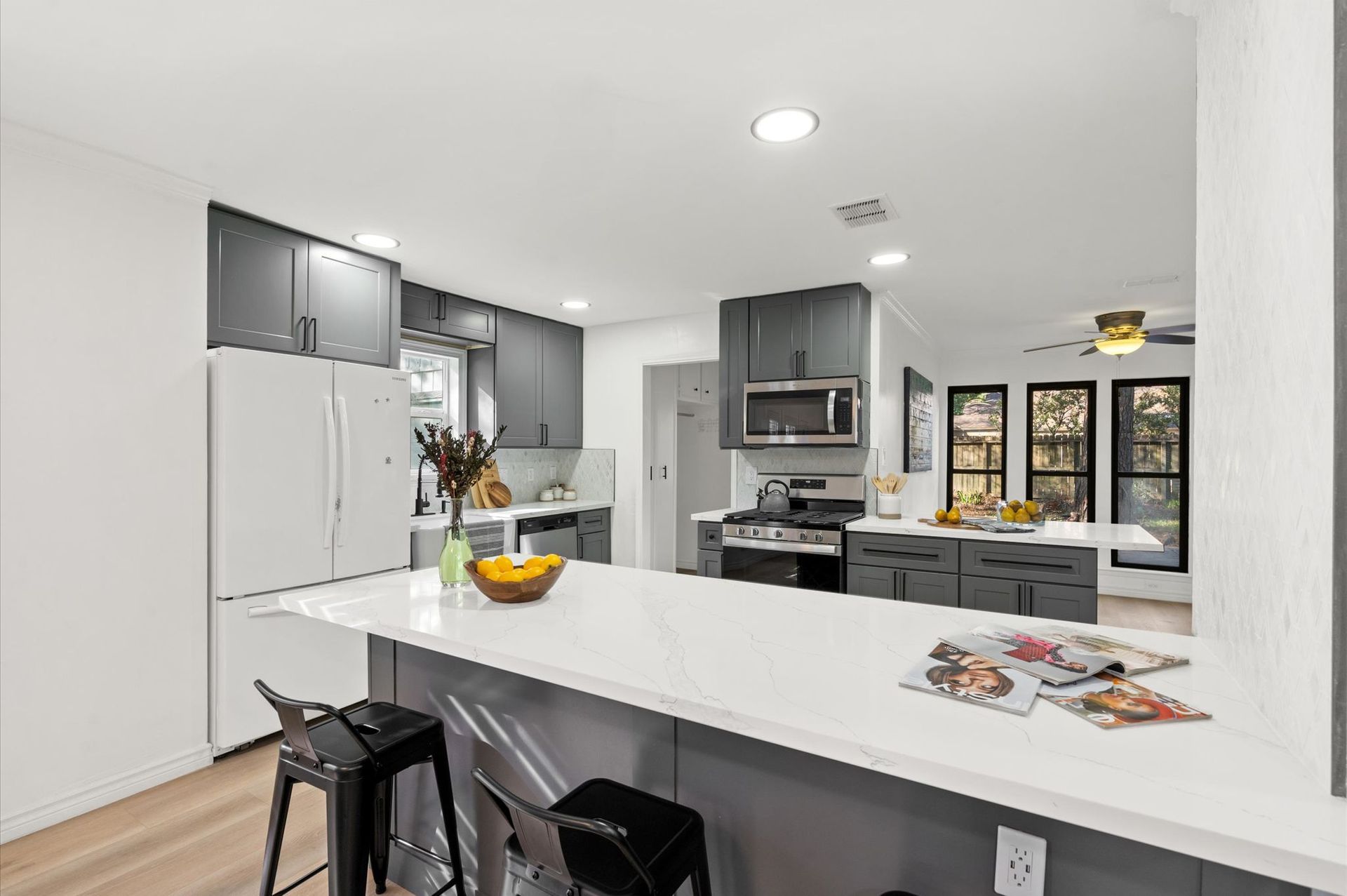 A kitchen with gray cabinets , white counter tops , stools and a large island.