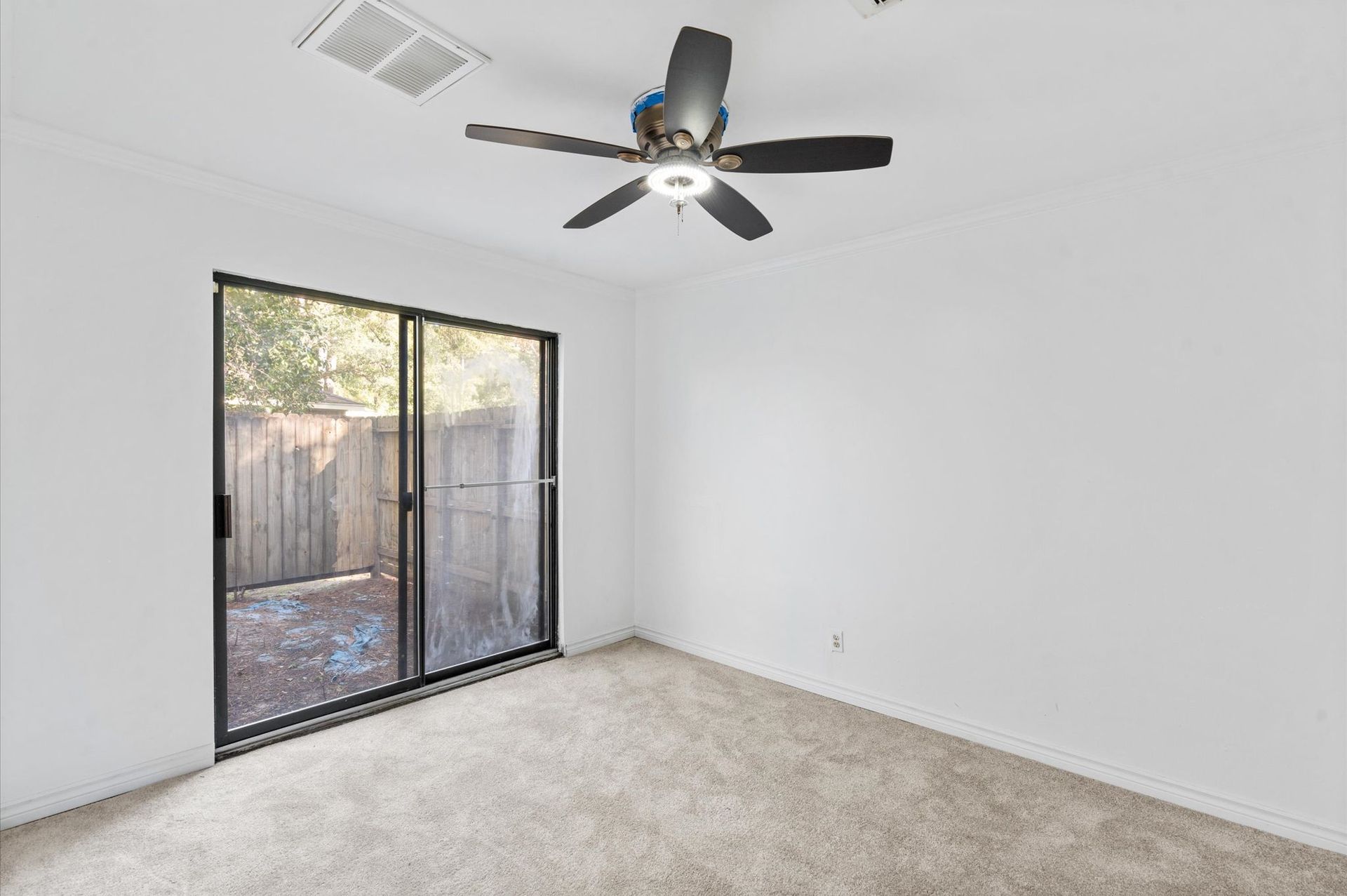An empty bedroom with a ceiling fan and sliding glass doors.