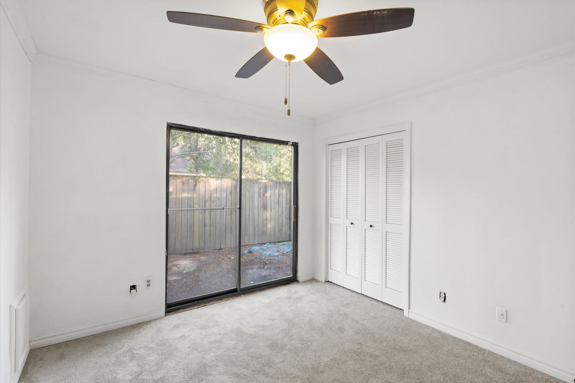 An empty room with a ceiling fan and sliding glass doors.
