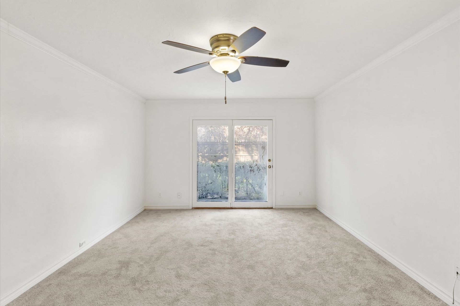 An empty living room with a ceiling fan and sliding glass doors.