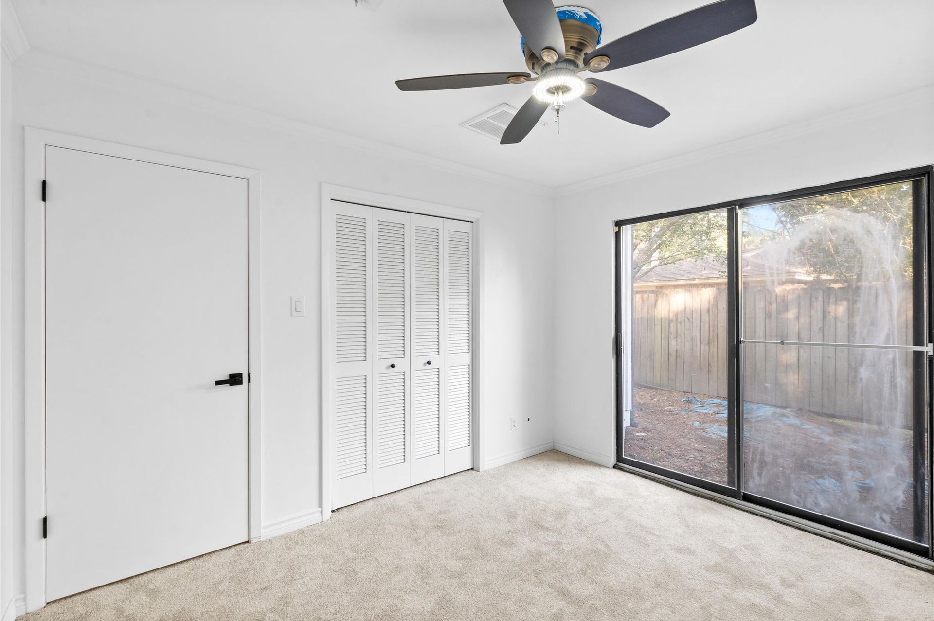 An empty room with a ceiling fan and sliding glass doors.