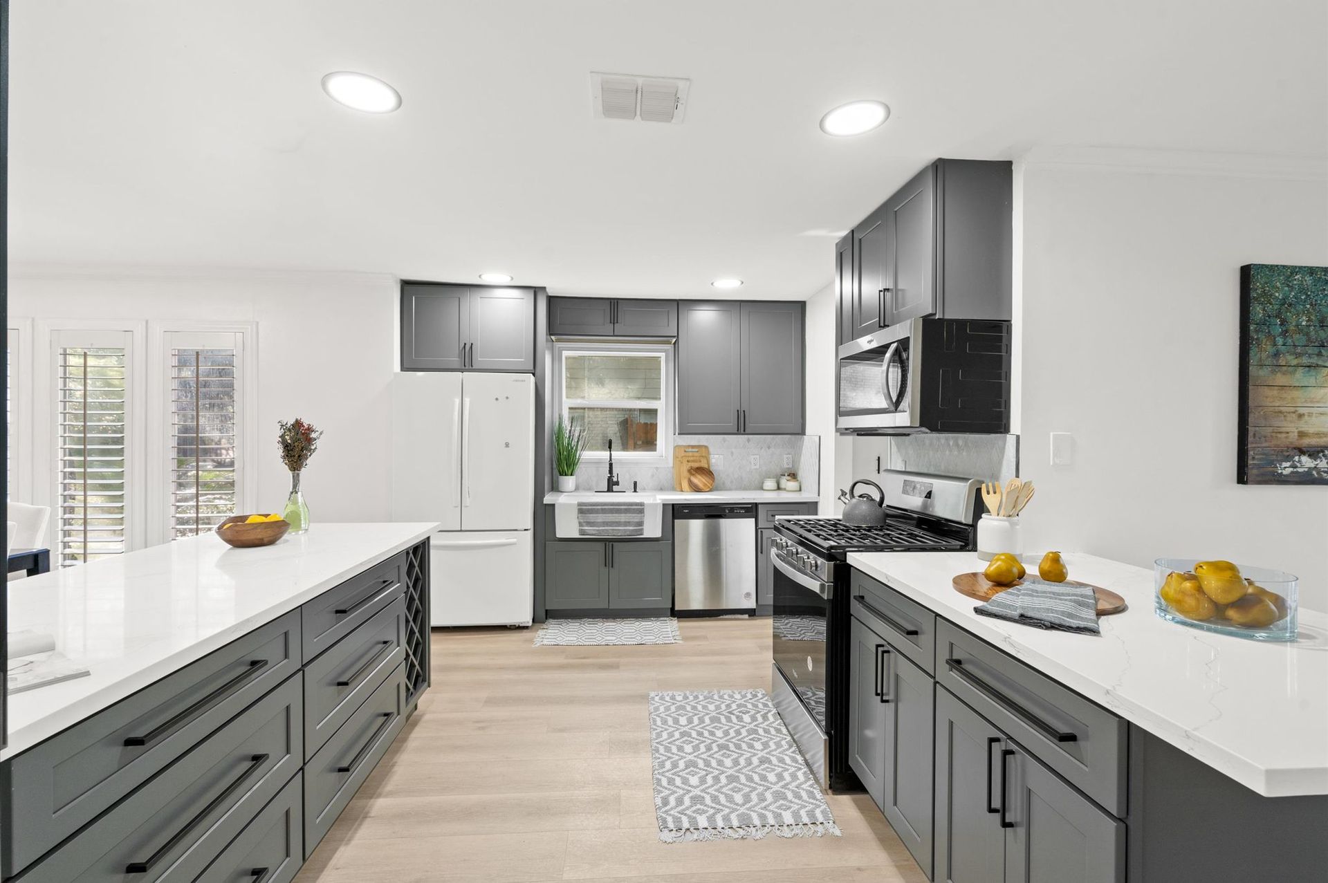 A kitchen with gray cabinets , white counter tops , stainless steel appliances and a large island.