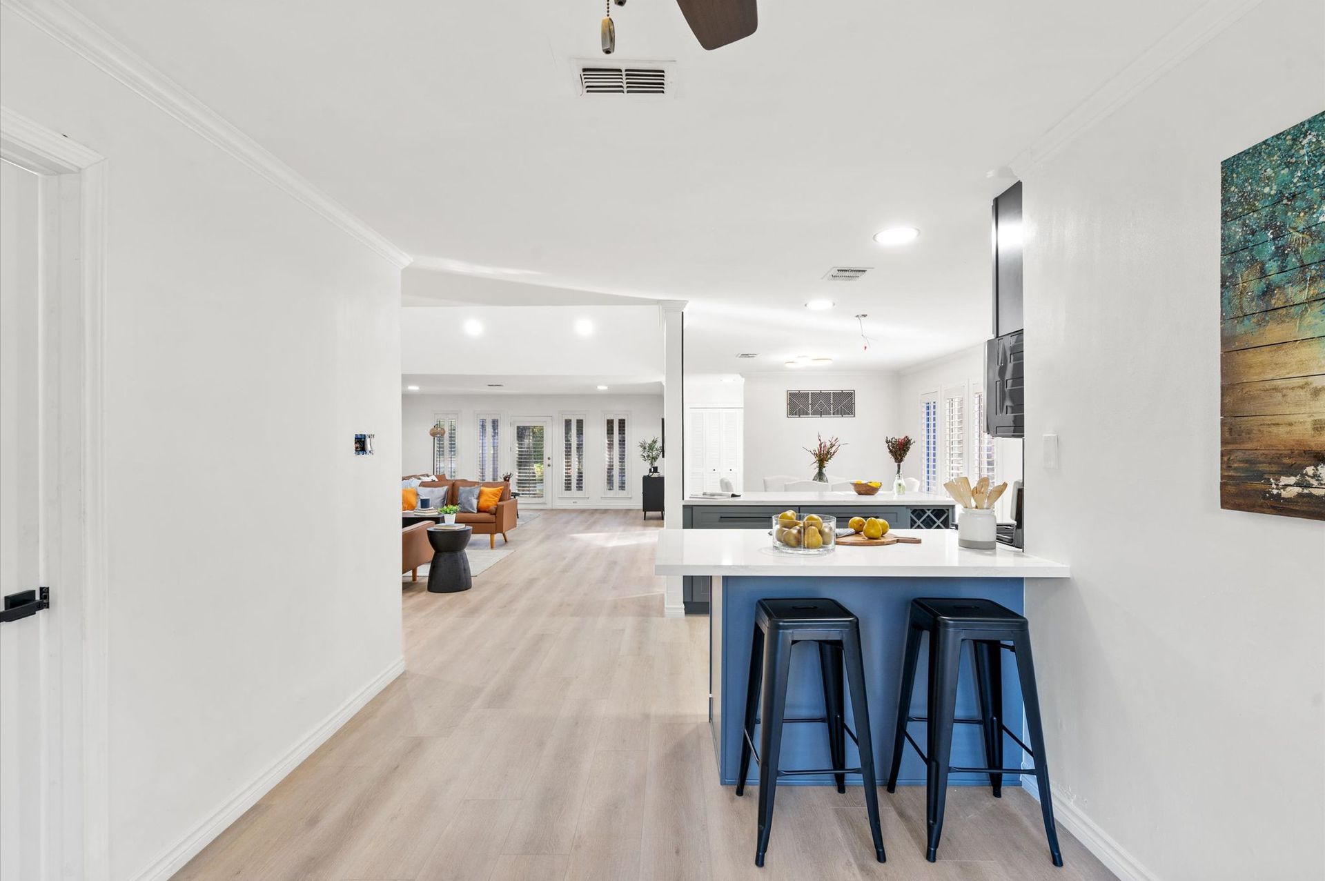A kitchen with a blue island and stools and a ceiling fan.