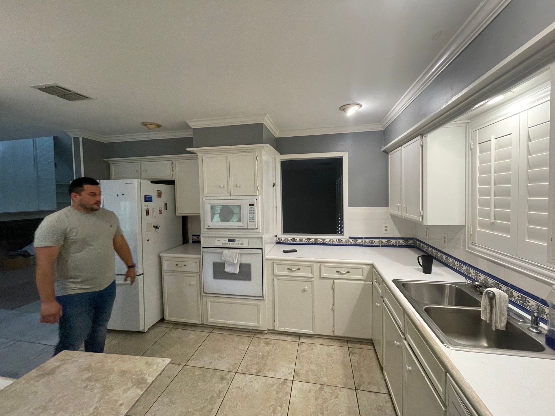 A man is standing in a kitchen with white cabinets and a sink.