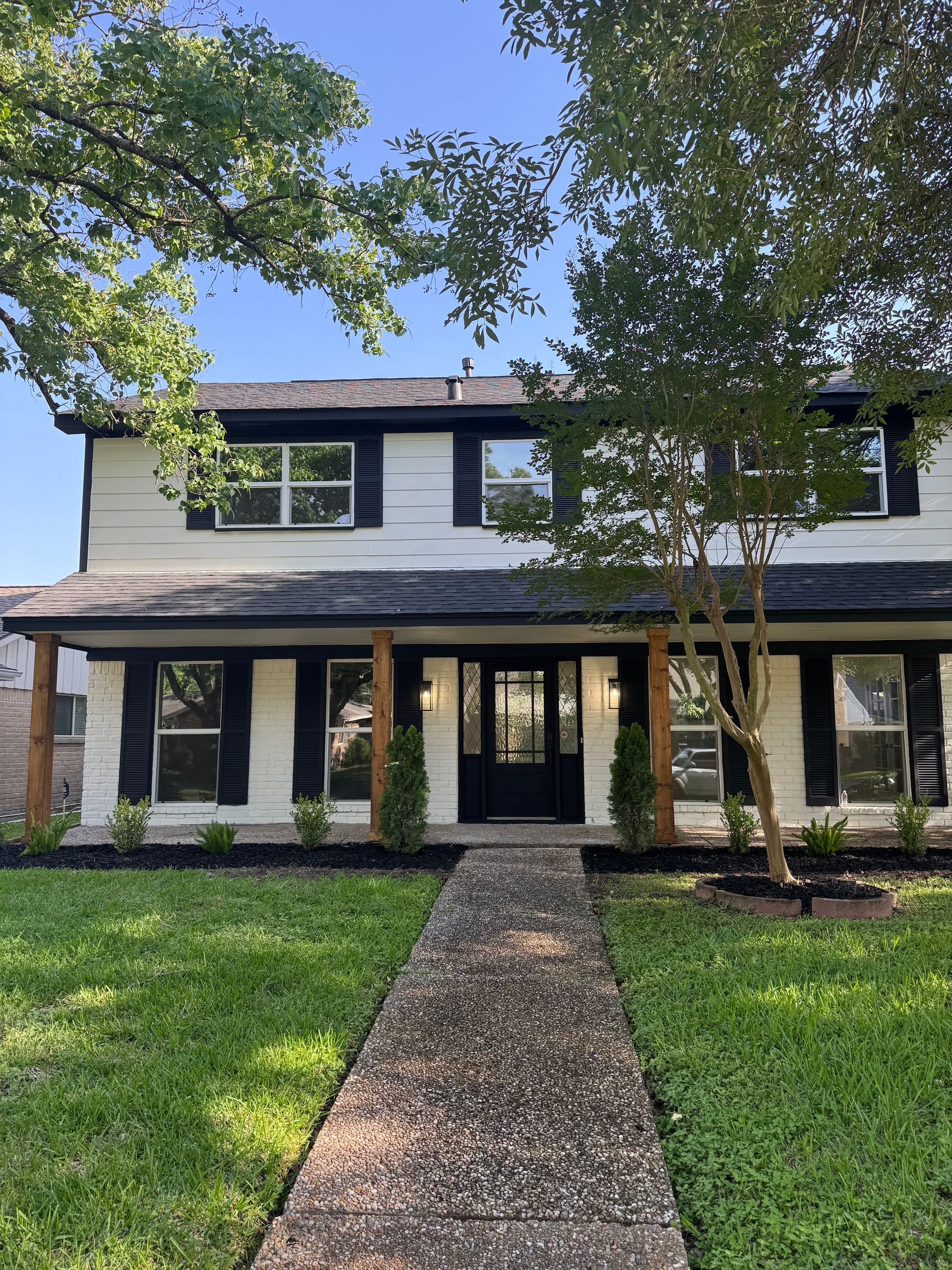 Two-story white house with black shutters, a concrete walkway, and a green lawn.