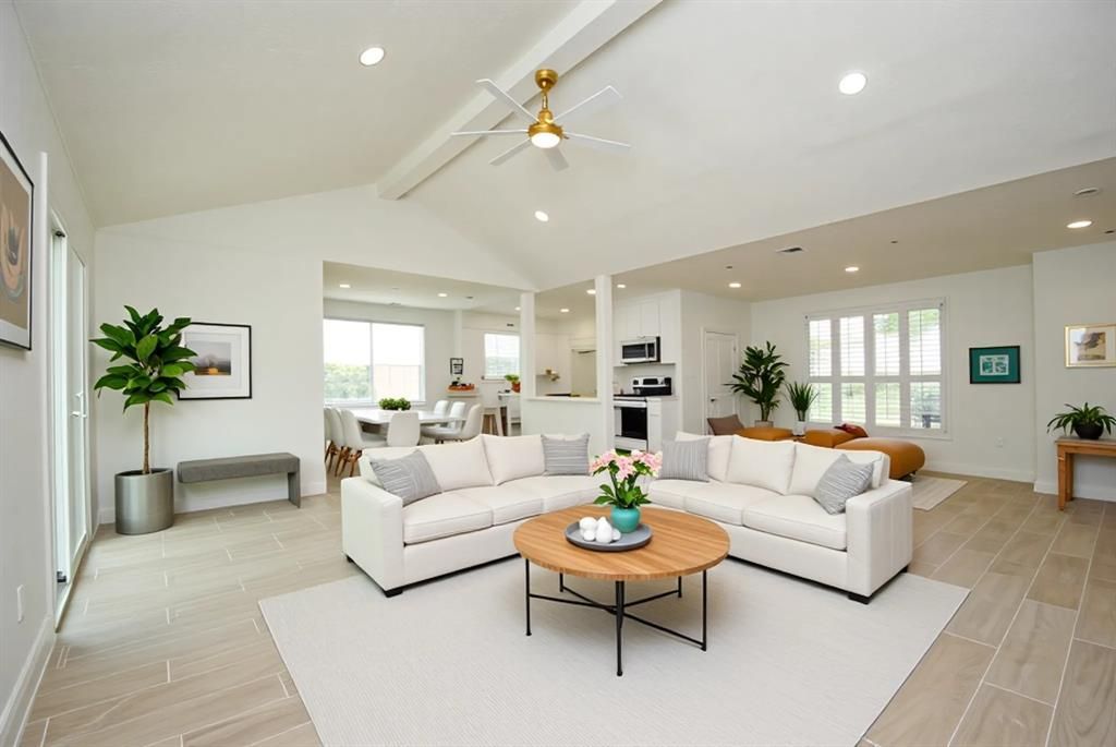 Spacious white living room with sectional sofa, round coffee table, and vaulted ceiling.