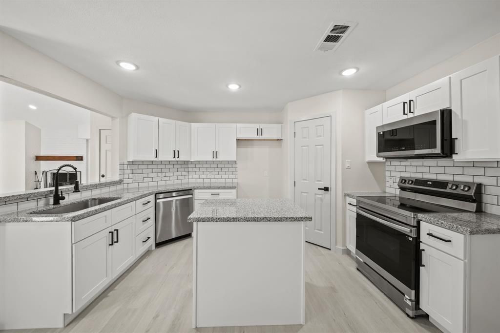 Modern white kitchen with stainless steel appliances and gray countertops.