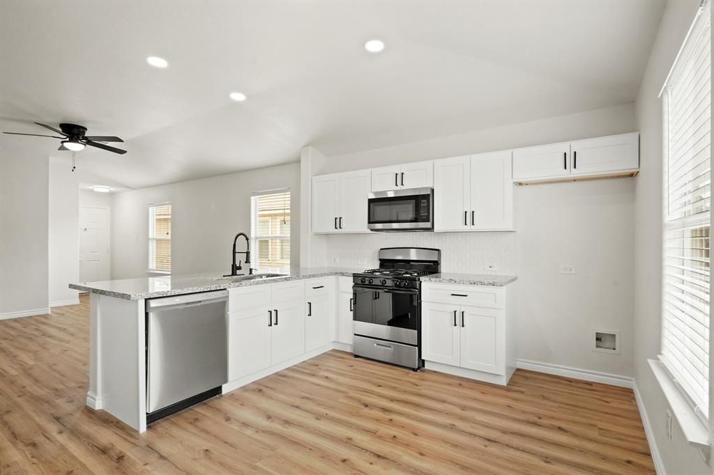 Modern, bright kitchen with white cabinets, stainless steel appliances, and wooden floors.