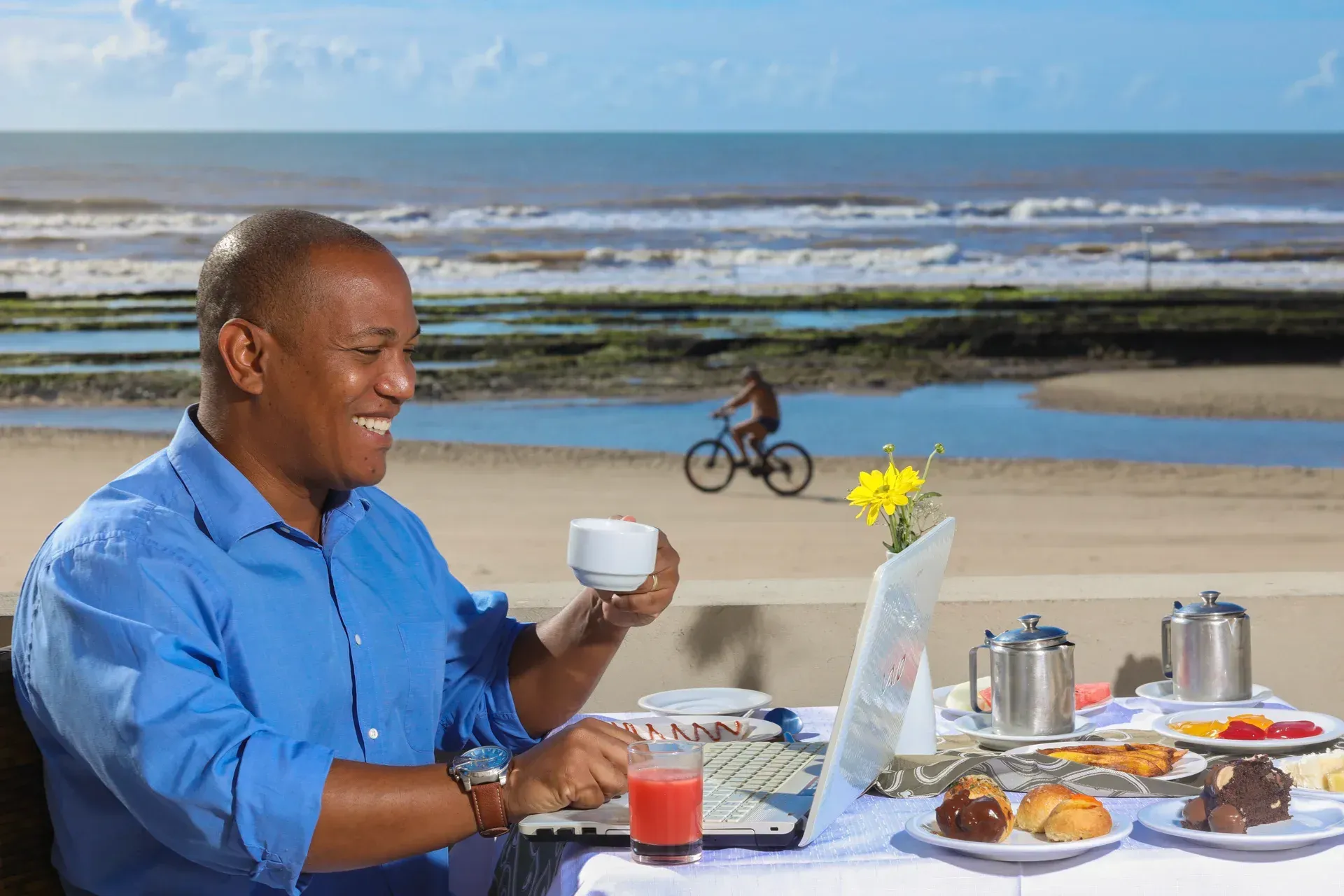 Um homem está sentado a uma mesa com um laptop e uma xícara de café.
