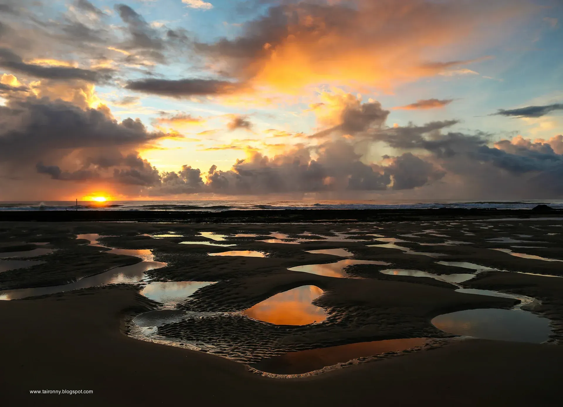 Um pôr do sol sobre uma praia com poças na areia