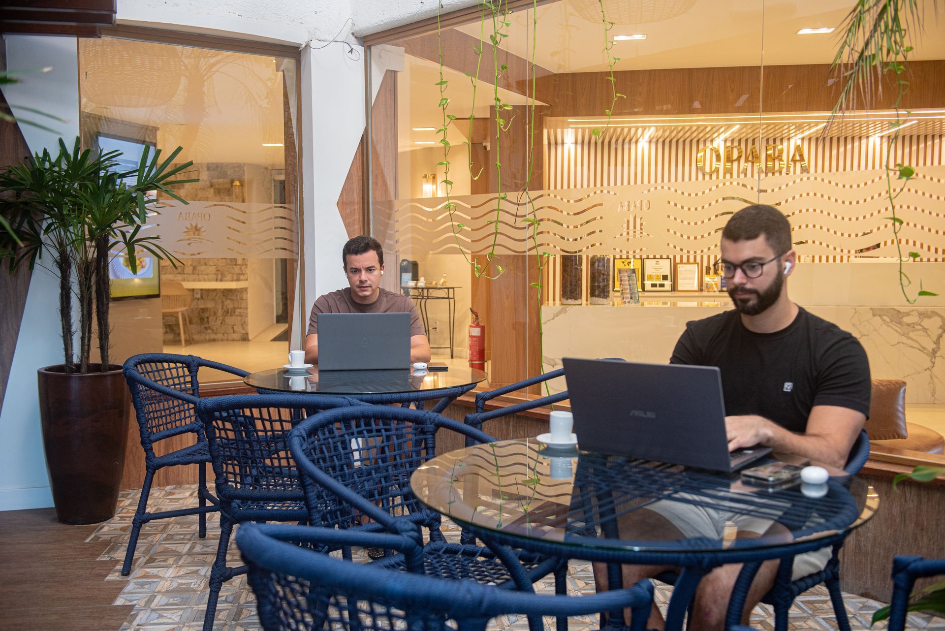 Um homem está sentado a uma mesa com um laptop e uma xícara de café.