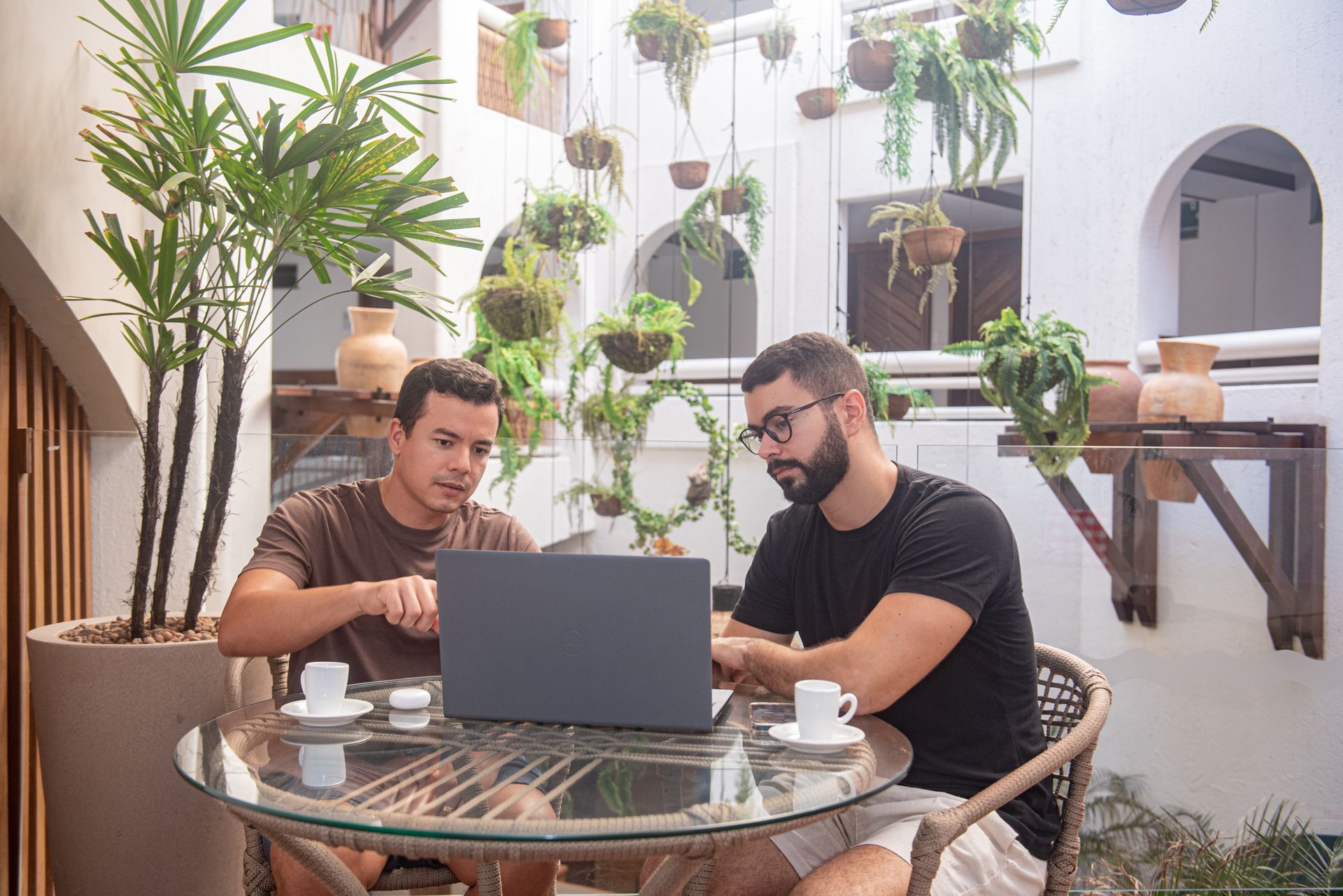 Dois homens estão apertando as mãos enquanto estão sentados em uma mesa com laptops.