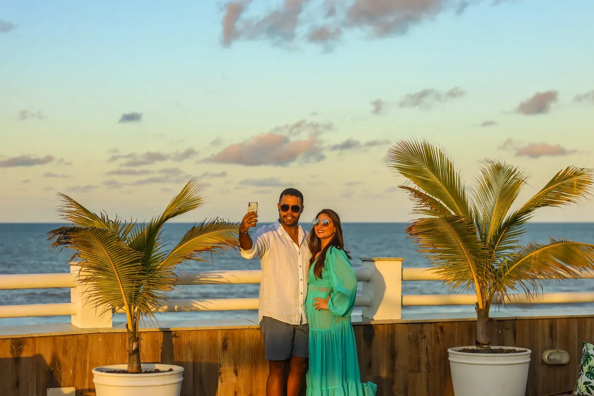 Um homem e uma mulher estão tirando uma selfie em uma varanda com vista para o oceano.