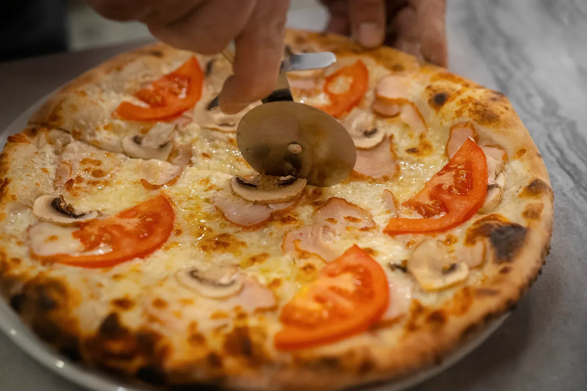Uma pessoa está cortando uma pizza com um cortador de pizza.