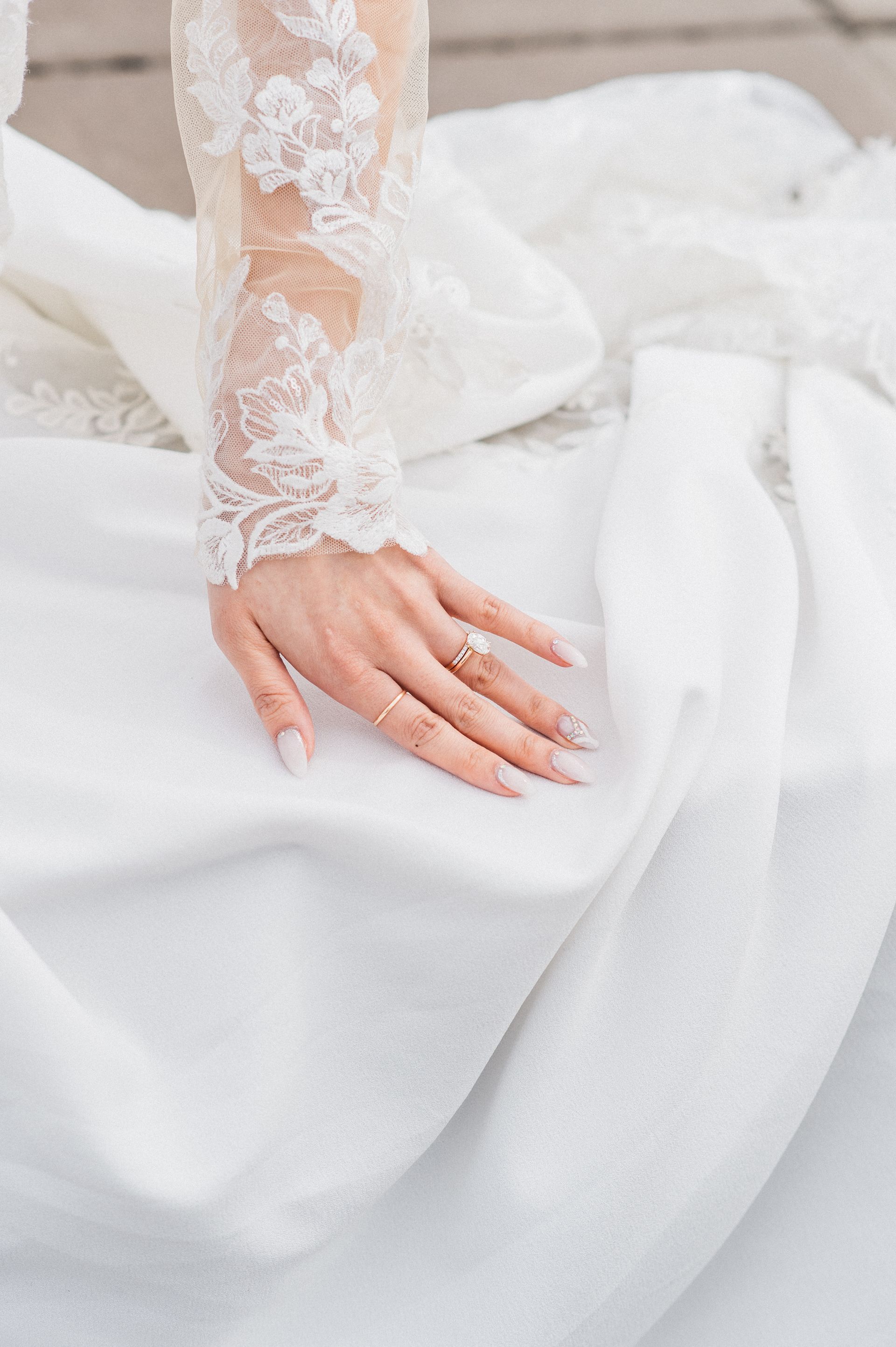 Hand on white fabric with lace sleeve, wearing a ring.