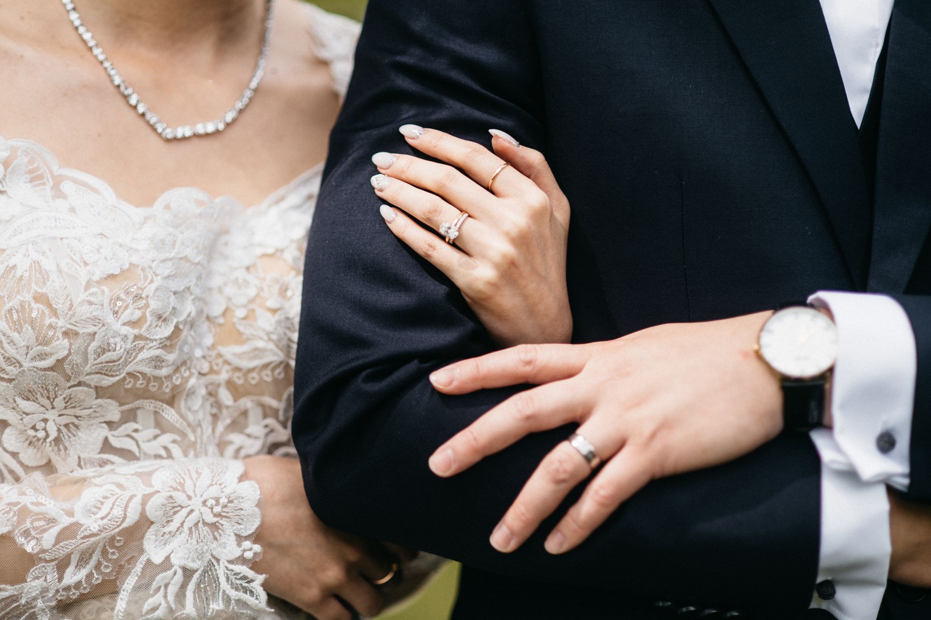 Bride's hand on groom's arm. Both wearing rings, bride in lace dress, groom in suit.