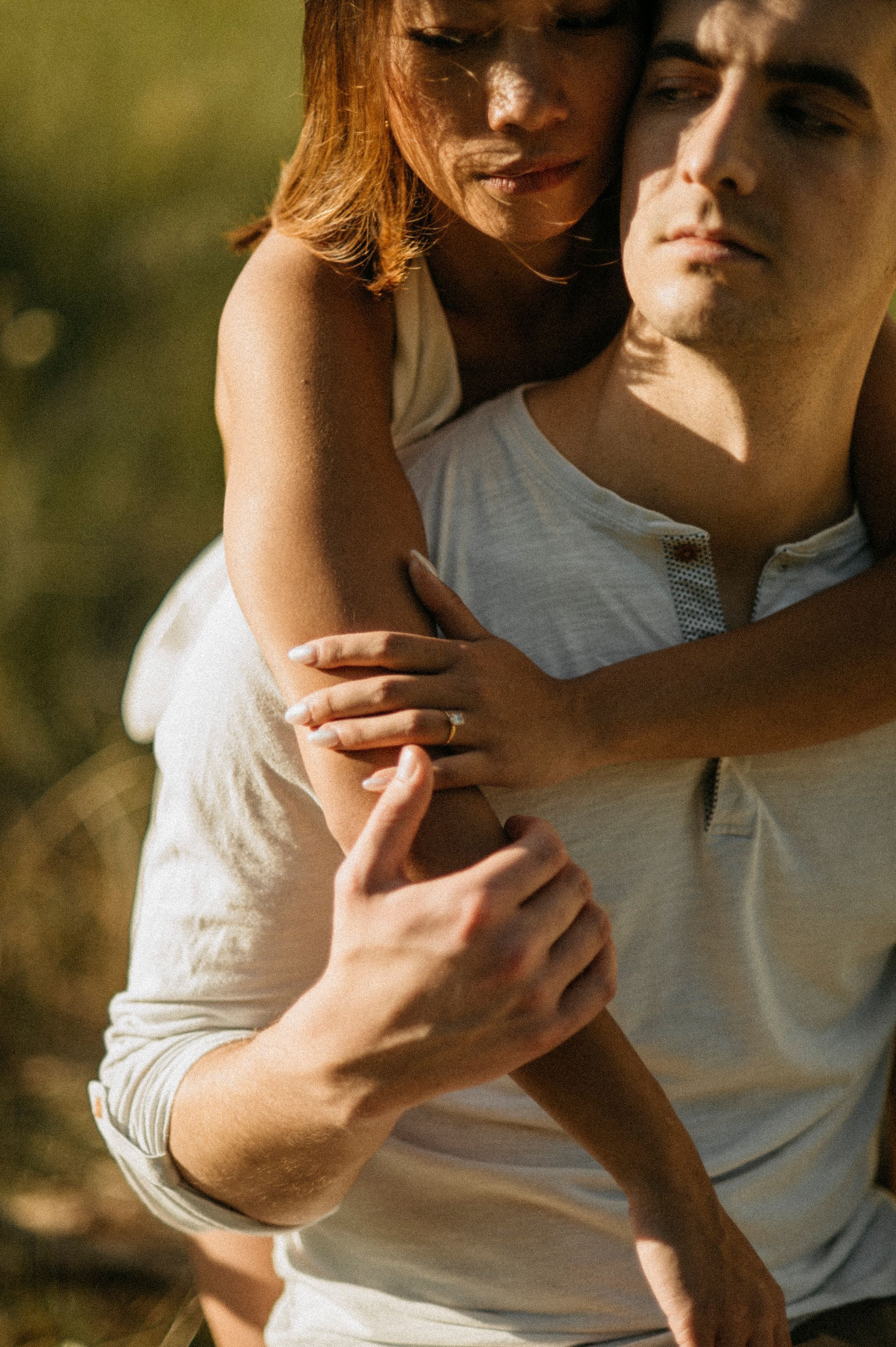 Woman hugging a man from behind outdoors. Warm sunlight, soft focus.