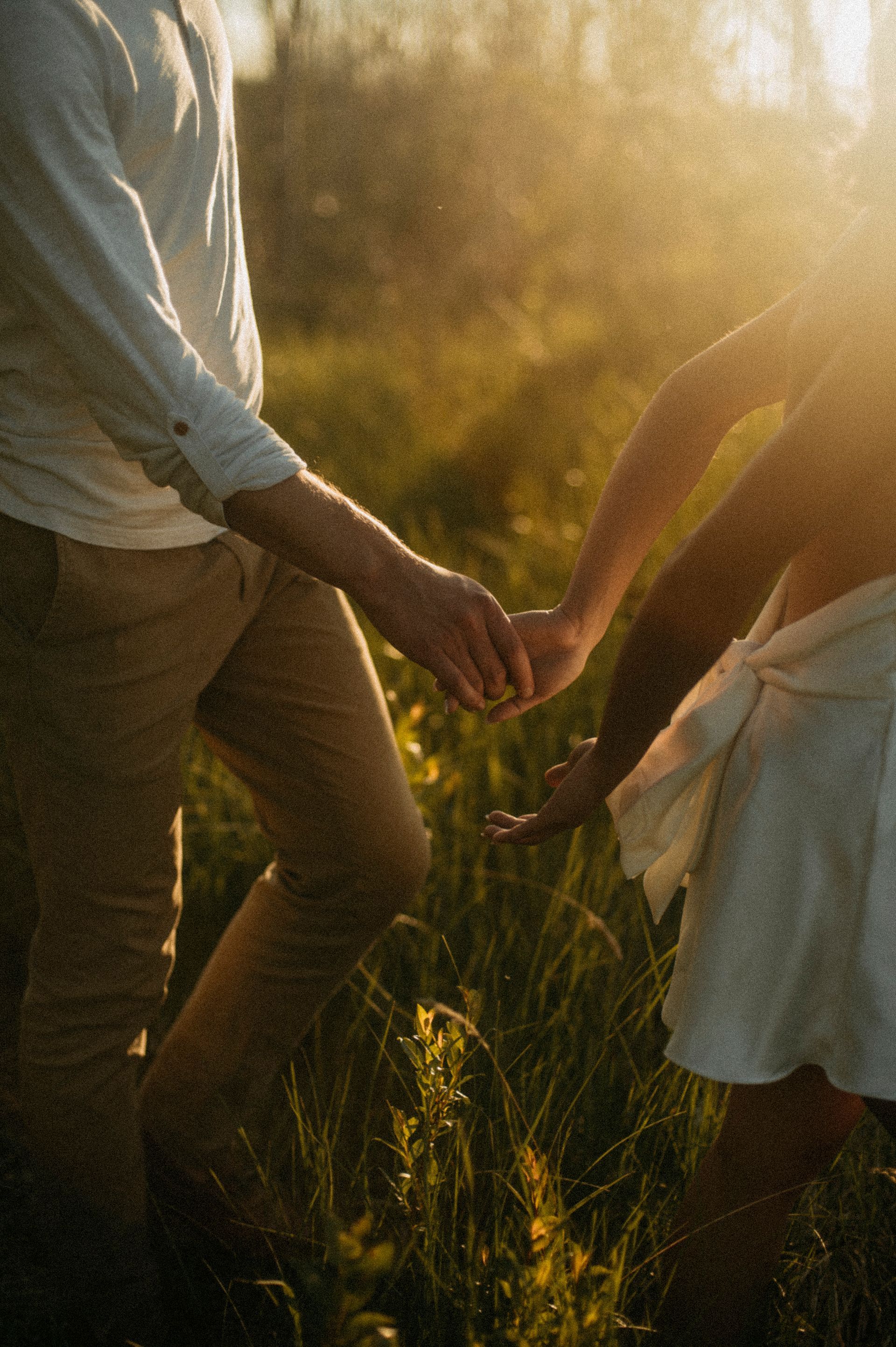 Couple holding hands, walking in a grassy field, sunlit, warm tones.