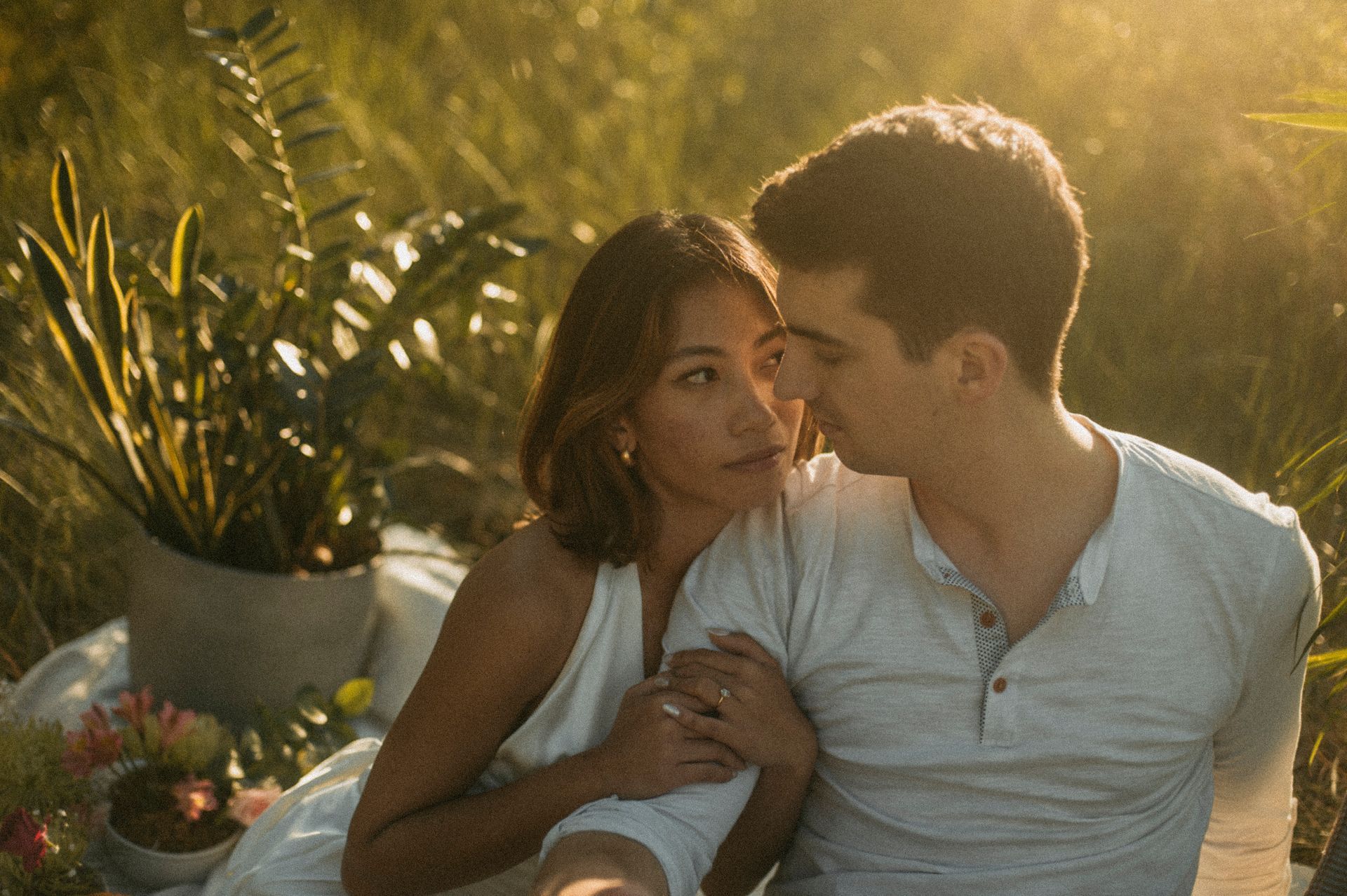 Couple embracing outdoors, golden light, picnic blanket, plants.