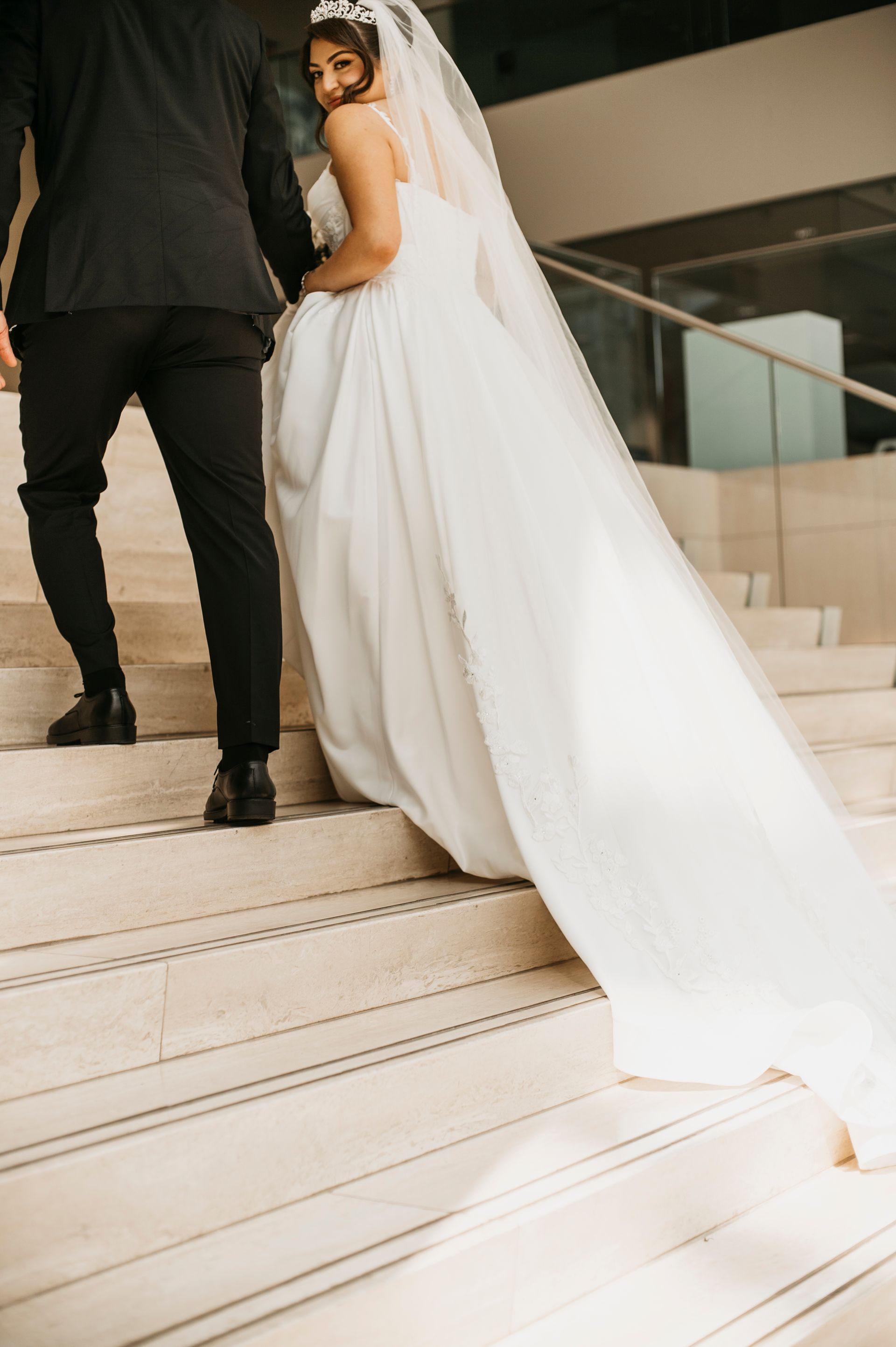 Bride in a white gown and veil walking up stairs with a person in a black suit.