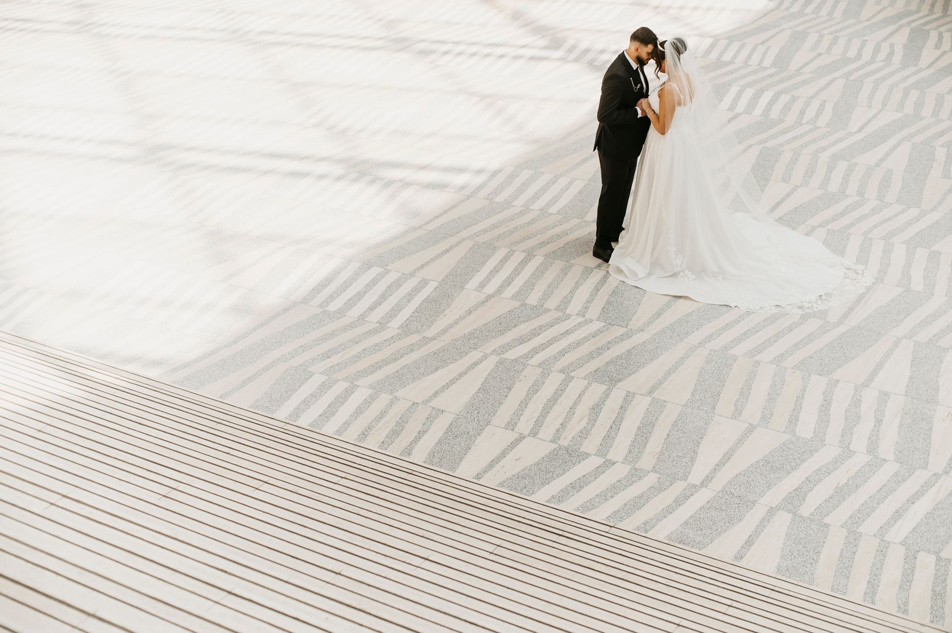 Couple in wedding attire on a geometric carpet. Groom in a black suit, bride in white dress and veil.