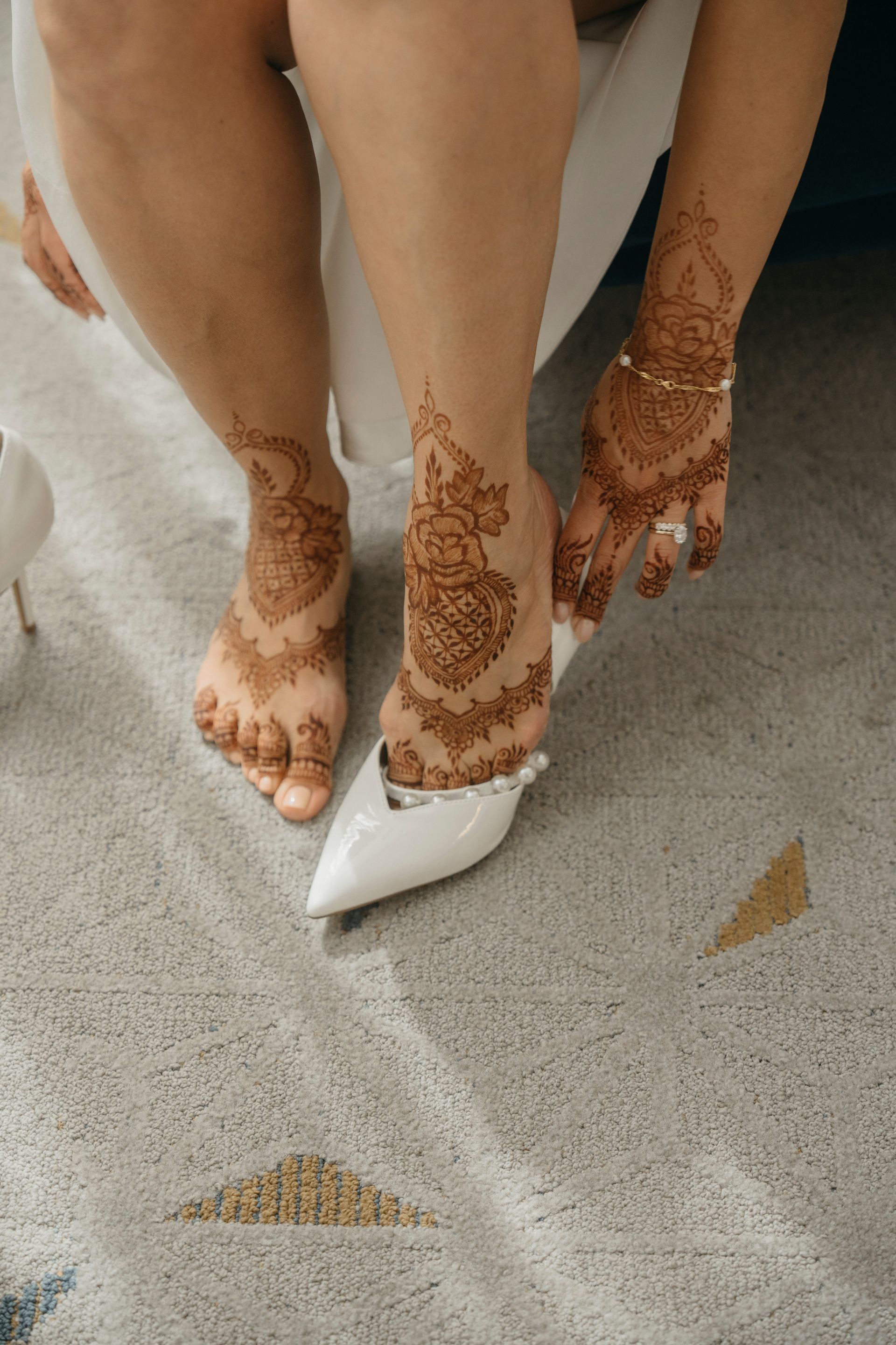 Person putting on a white shoe, with henna art on their feet and hand.