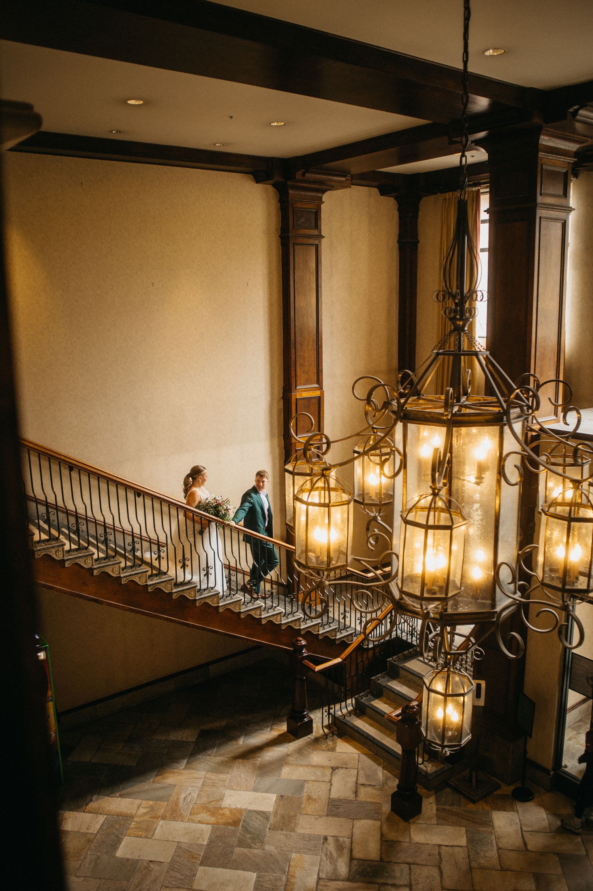 Couple on a grand staircase, descending beneath a large ornate chandelier.
